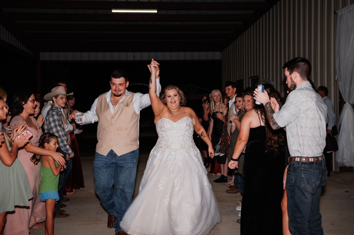 Bride and groom celebrate grand exit at rustic barn wedding reception surrounded by cheering guests.