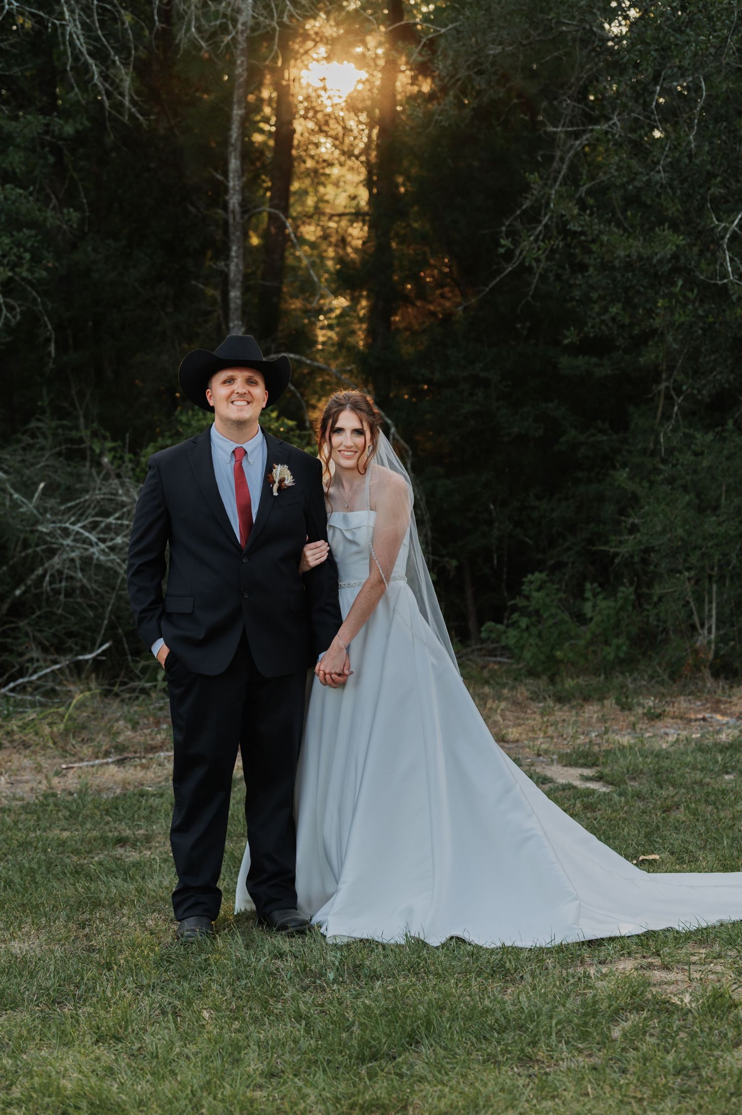 Bride and groom hold hands posing together at sunset in a wooded outdoor setting during their wedding.
