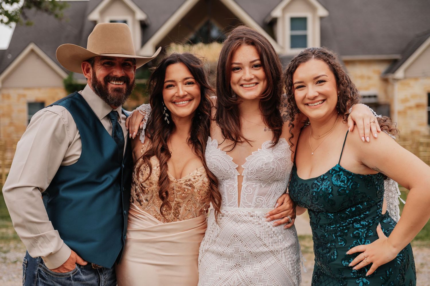 Four people smiling outdoors at a formal event, man in cowboy hat and vest with three women in elegant dresses.