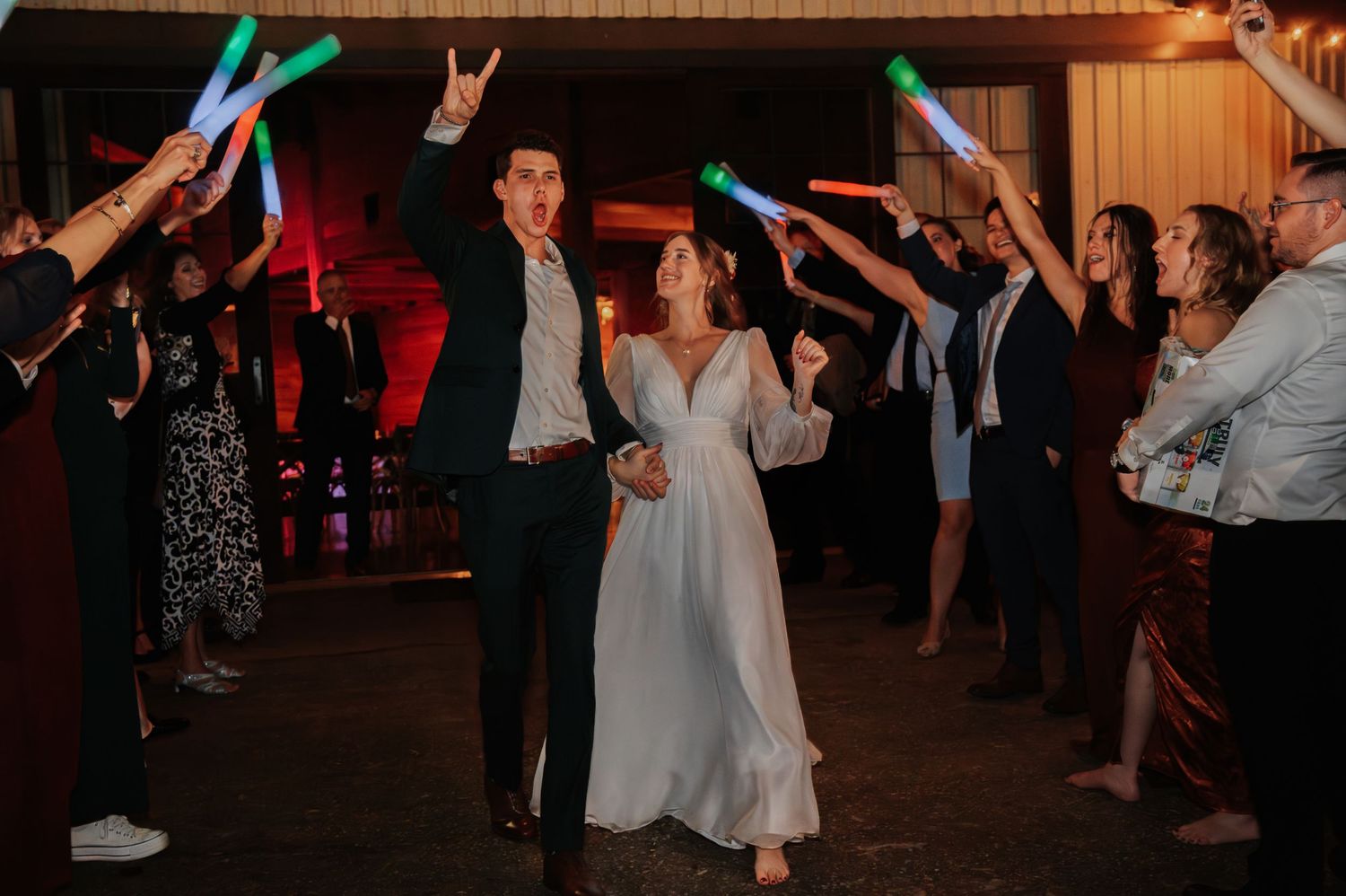 Bride and groom celebrate their reception exit with guests waving colorful LED light sticks in a festive send-off.