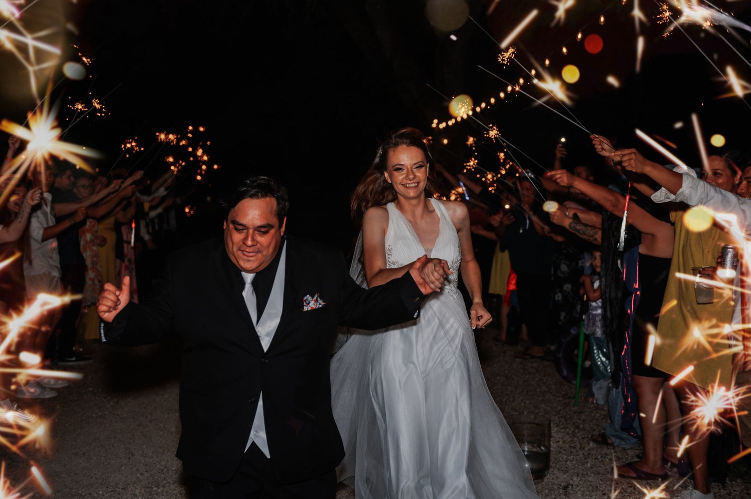 Bride and groom walk through sparkler tunnel at night wedding exit celebration.