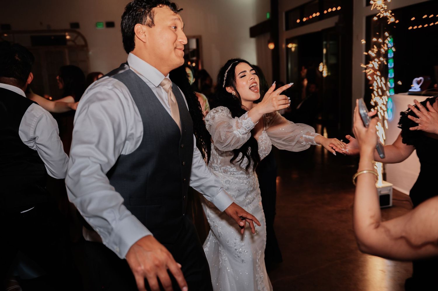 Bride and groom dancing joyfully with guests at a lively wedding reception celebration.