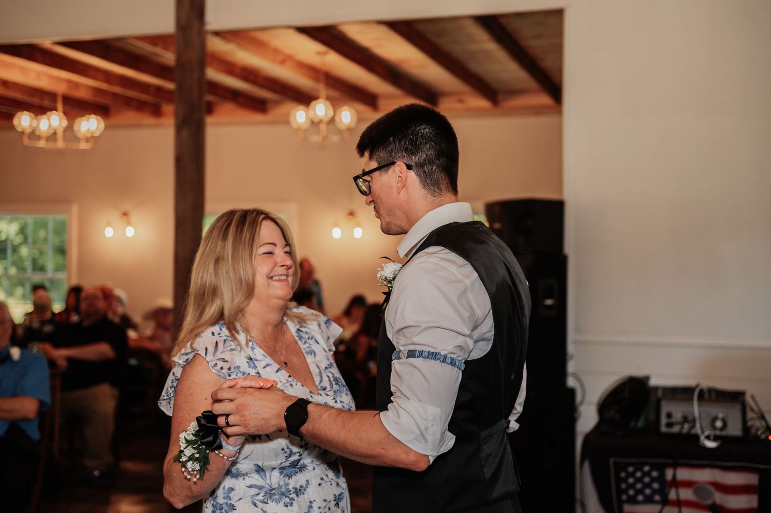 Groom dancing with his mother at a wedding reception in an elegant venue with chandeliers.