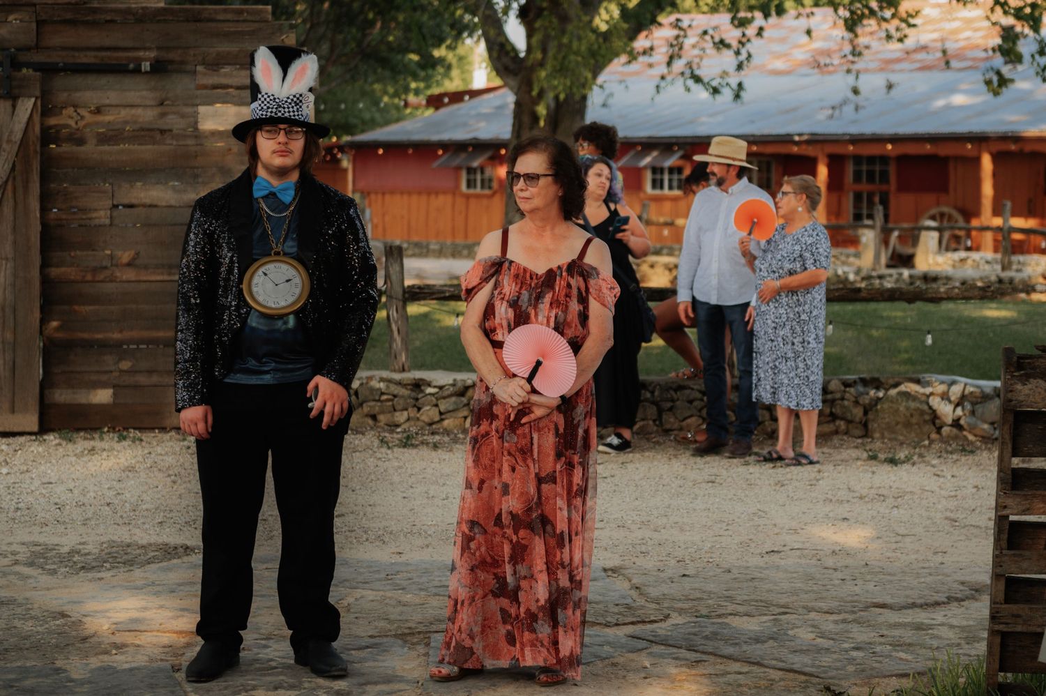 Couple in western attire poses outdoors at rustic barn venue during golden hour event.