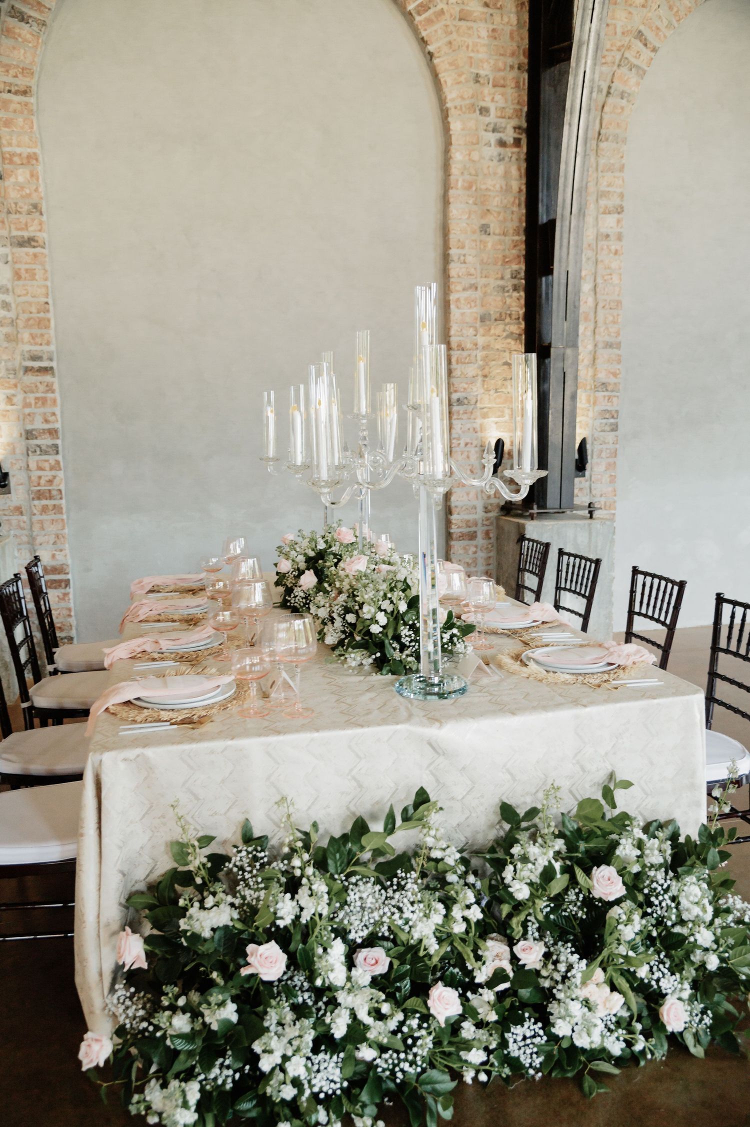 Wedding reception table with white floral runner, crystal candelabra centerpiece, and arched brick wall backdrop.
