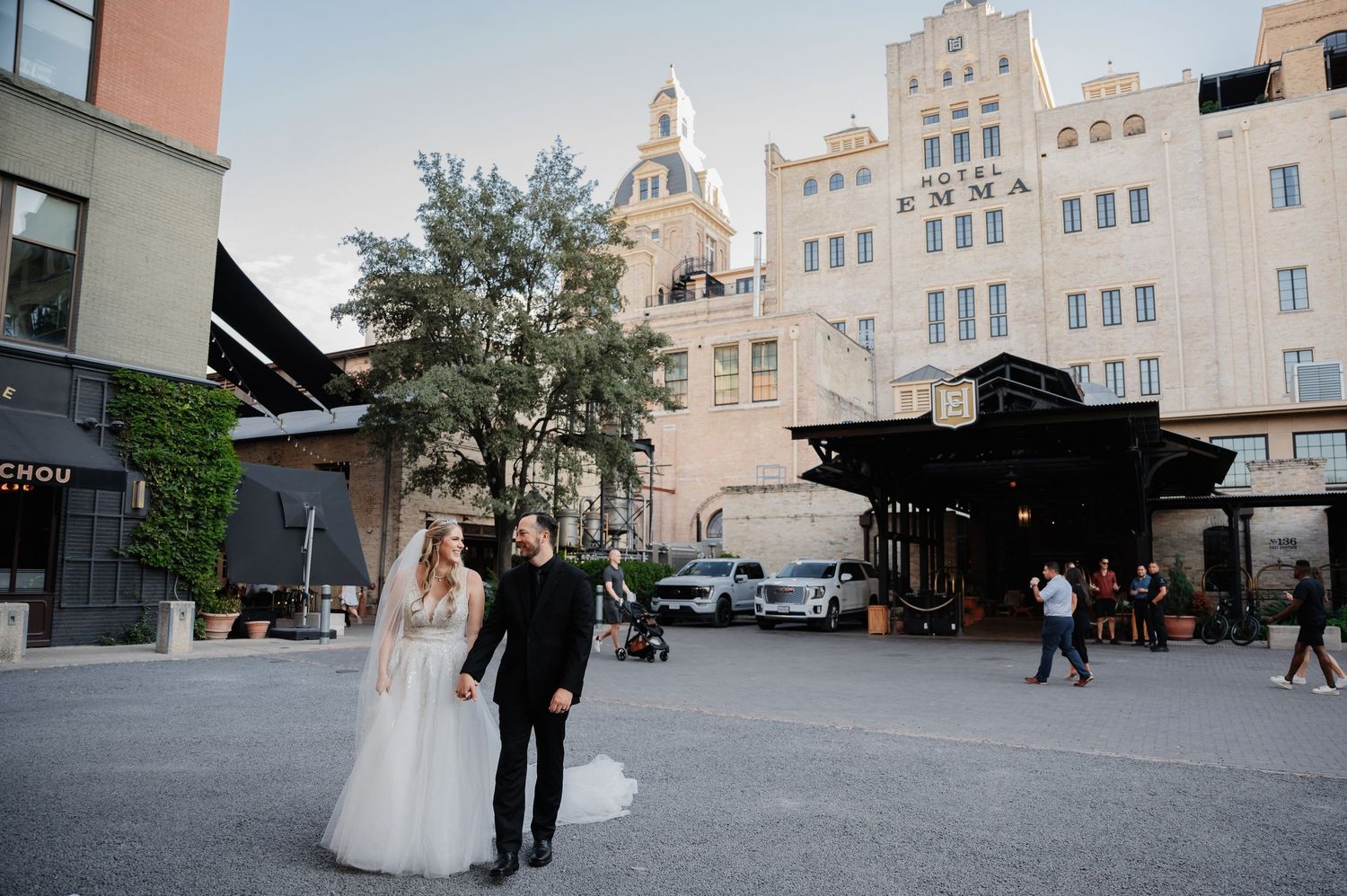 Bride and groom pose in an urban plaza with a historic white building backdrop on their wedding day.