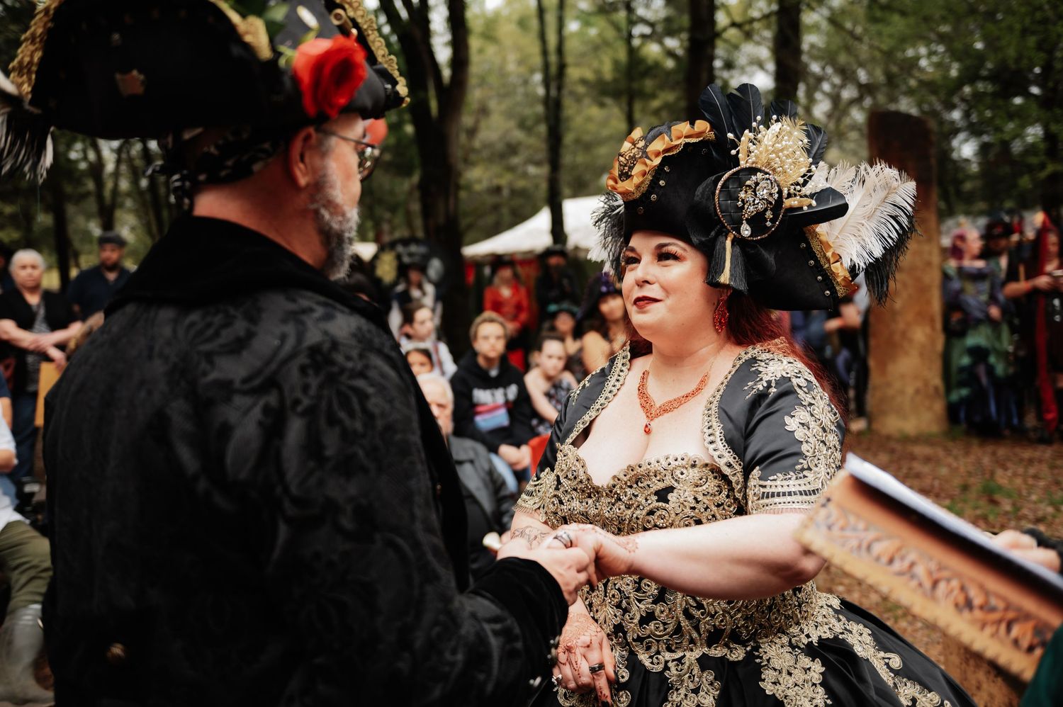 Couple in elaborate pirate costumes exchanging vows at a Renaissance faire outdoor wedding ceremony.