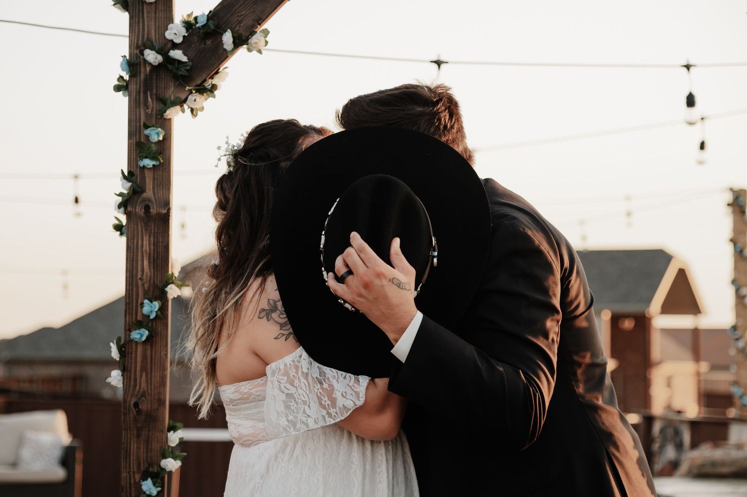 Bride and groom sharing first kiss under rustic wooden arch decorated with greenery at outdoor wedding ceremony.