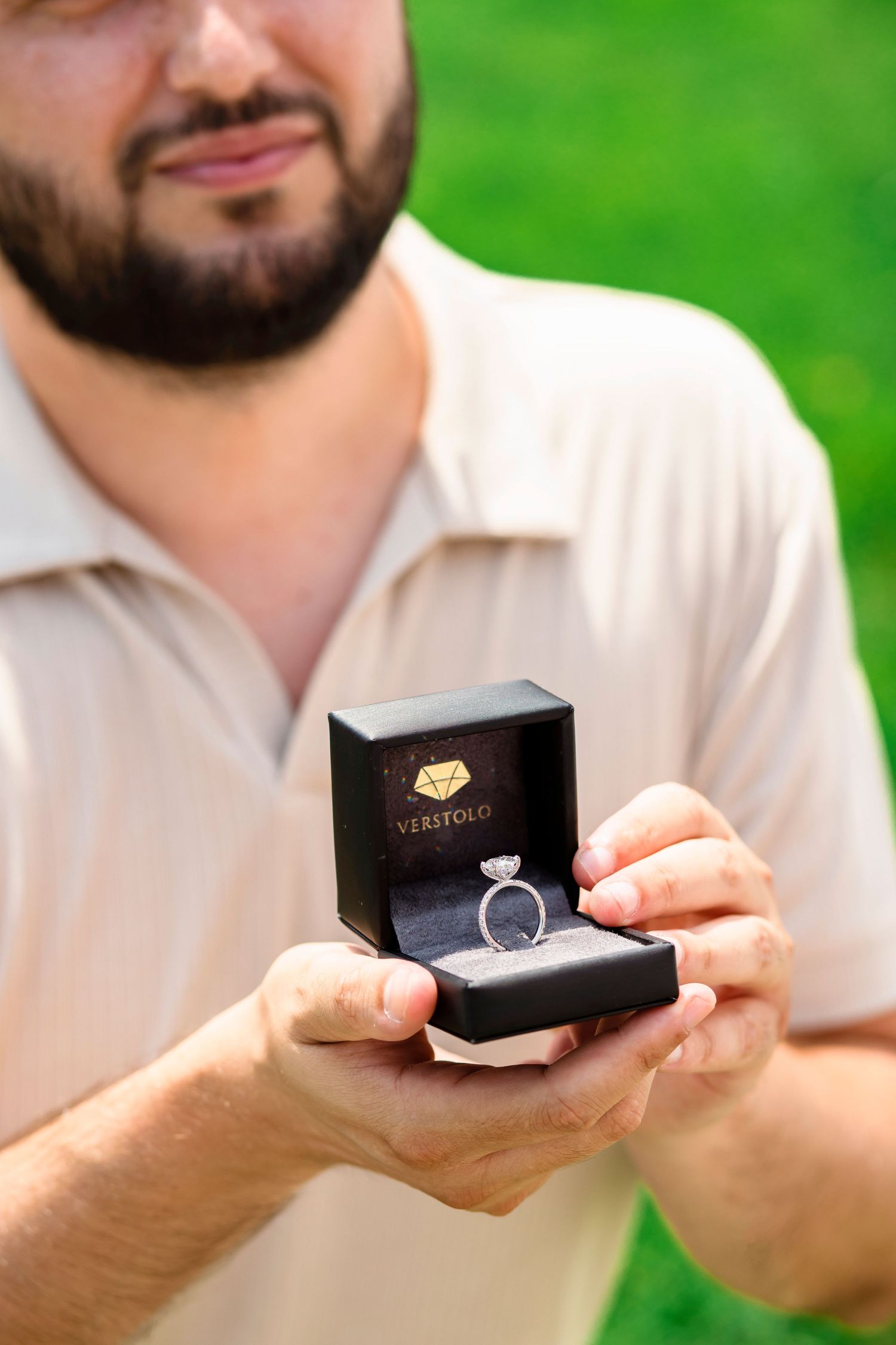 A sequence of hands holding a small black ring box with green foliage background.