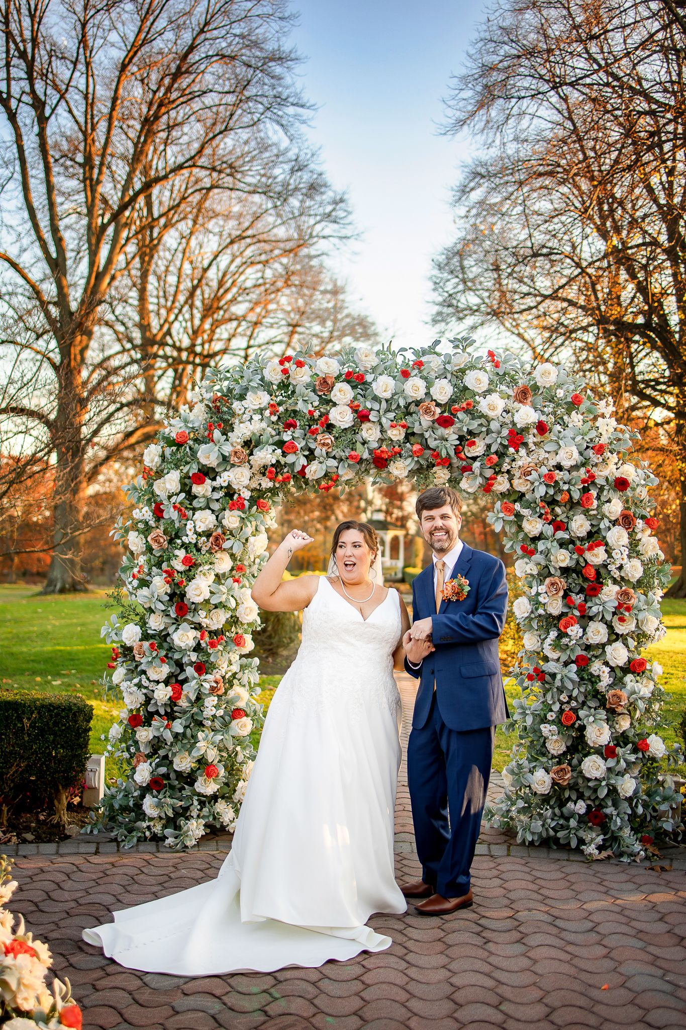 A stunning floral arch with red and white roses creates a magical wedding ceremony backdrop on a brick patio.