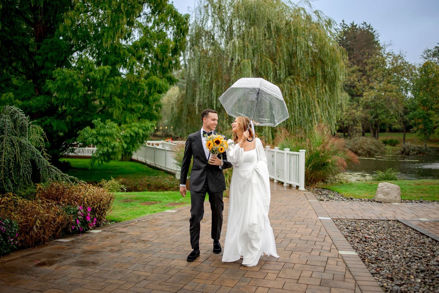 A couple walks together on a garden path under willow trees and flowering shrubs on a spring day.