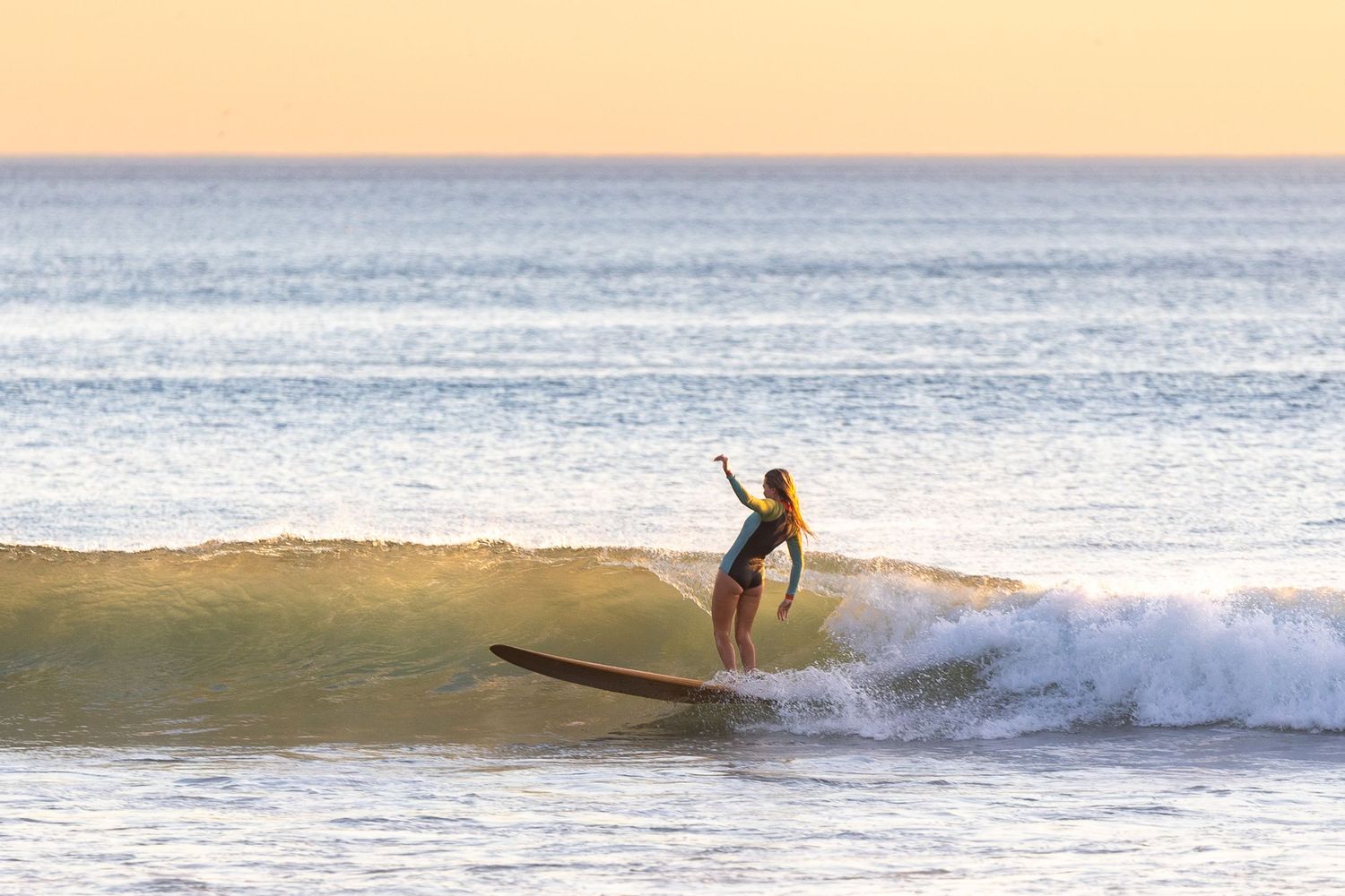 A surfer rides a wave during golden hour at sunset on a calm ocean beach.