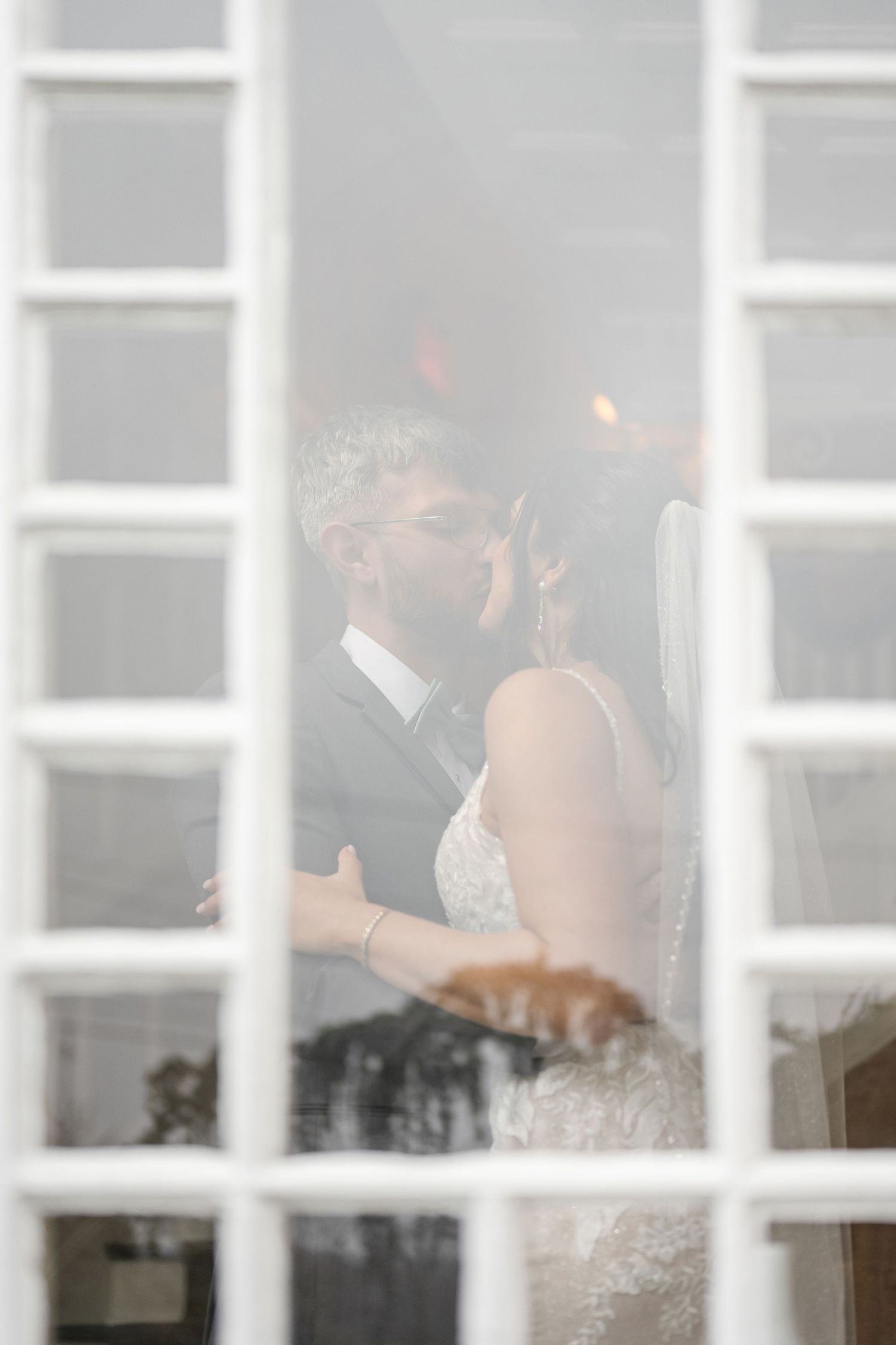 A romantic scene of newlyweds sharing a tender moment, viewed through white window panes with a soft dreamy focus.