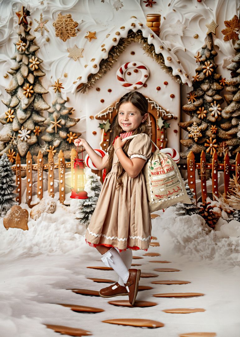 Little girl in a tan dress holds a lantern and North Pole sack in a magical gingerbread Christmas scene.