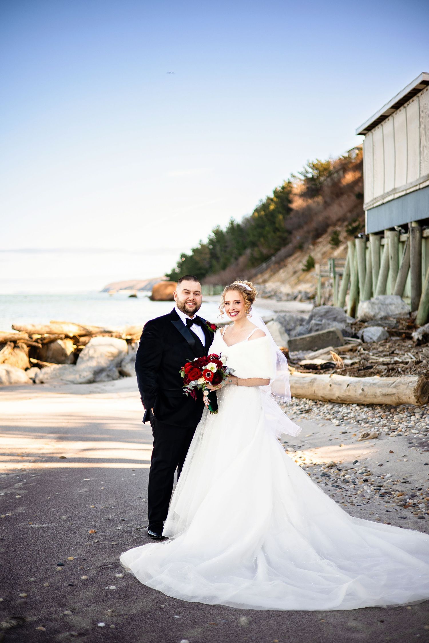 A couple in wedding attire poses together on a beach at sunset with flowing white dress and romantic atmosphere.