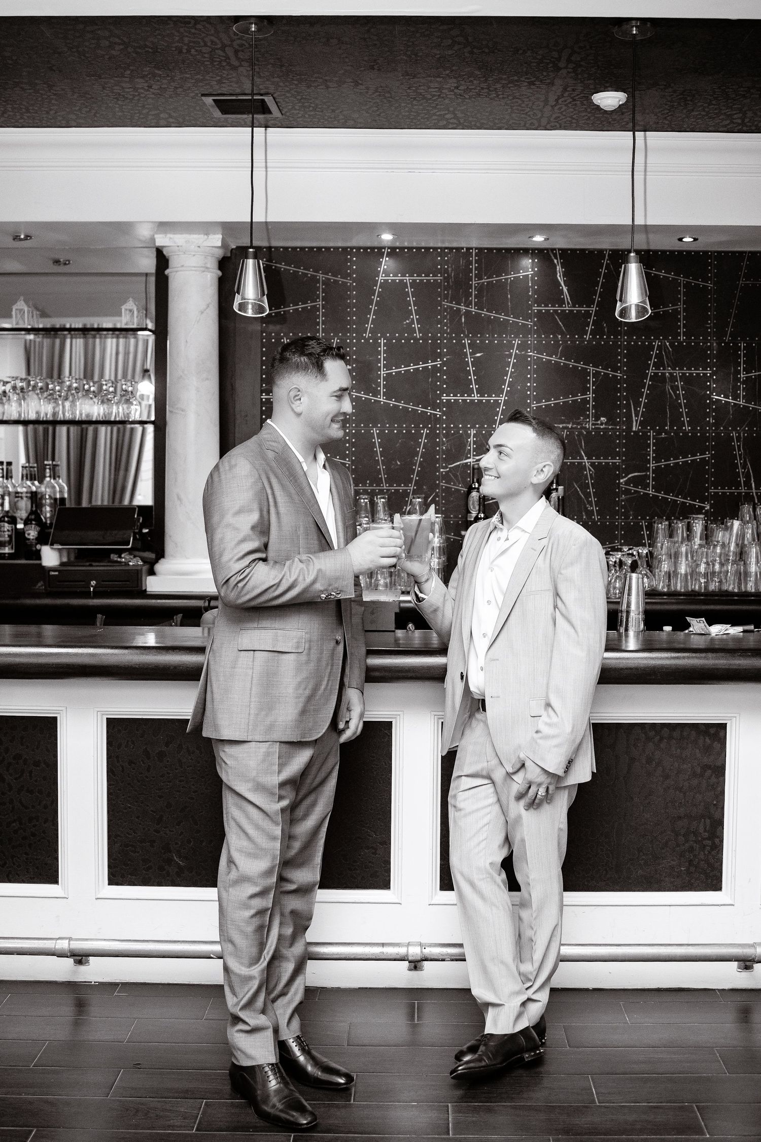 Two men in suits having a conversation while standing at a modern bar counter in black and white photography.