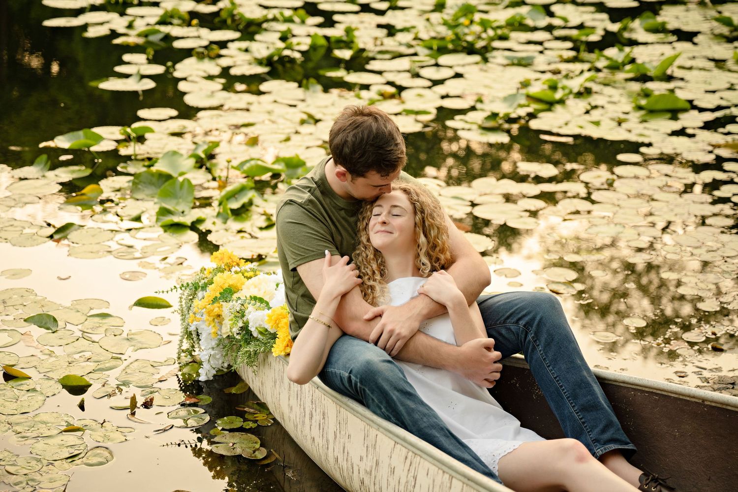 Romantic couple embracing in a wooden rowboat surrounded by lily pads on a serene pond.