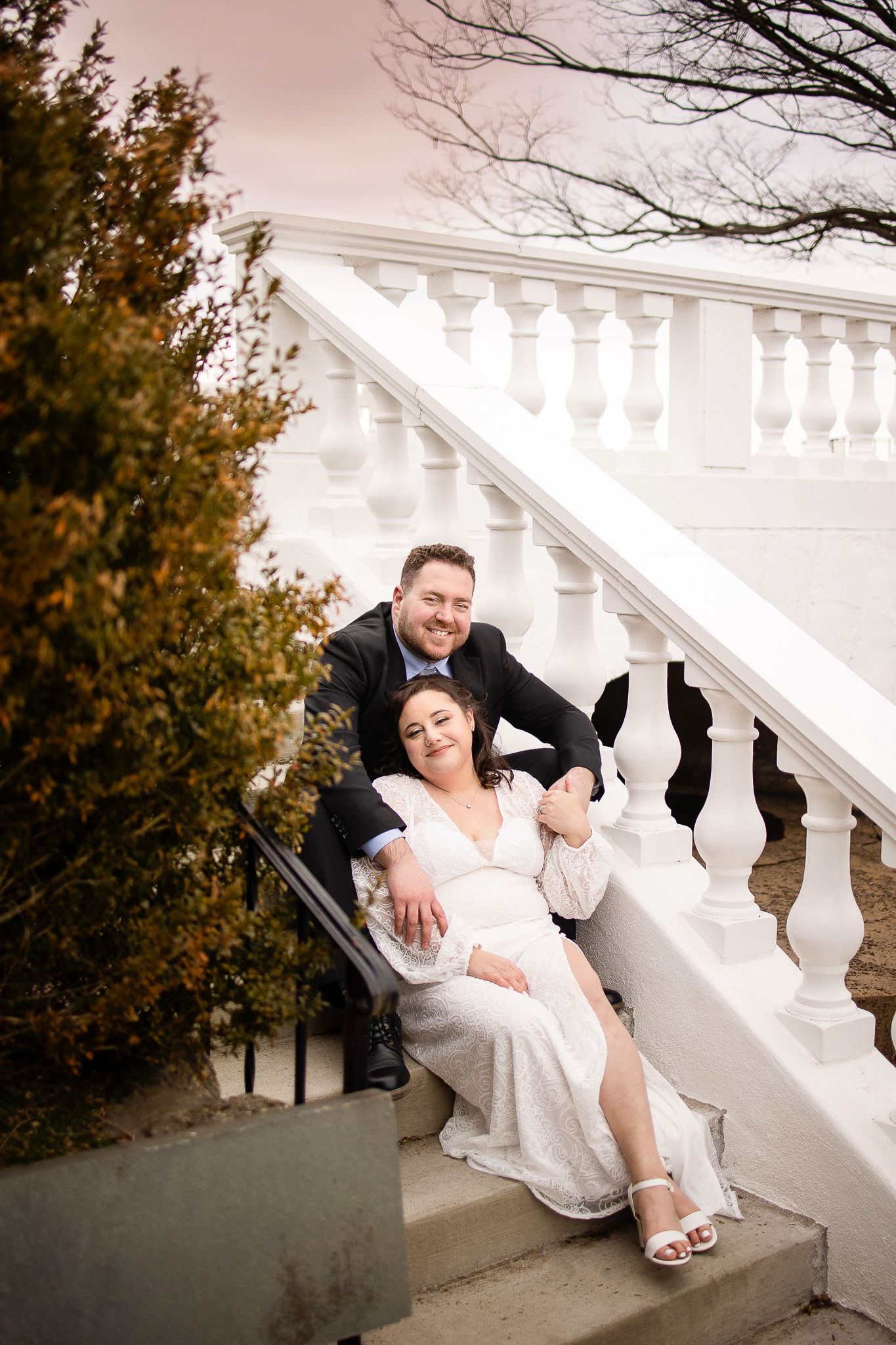 A couple poses together on elegant white stone stairs during autumn with decorative balusters in the background.