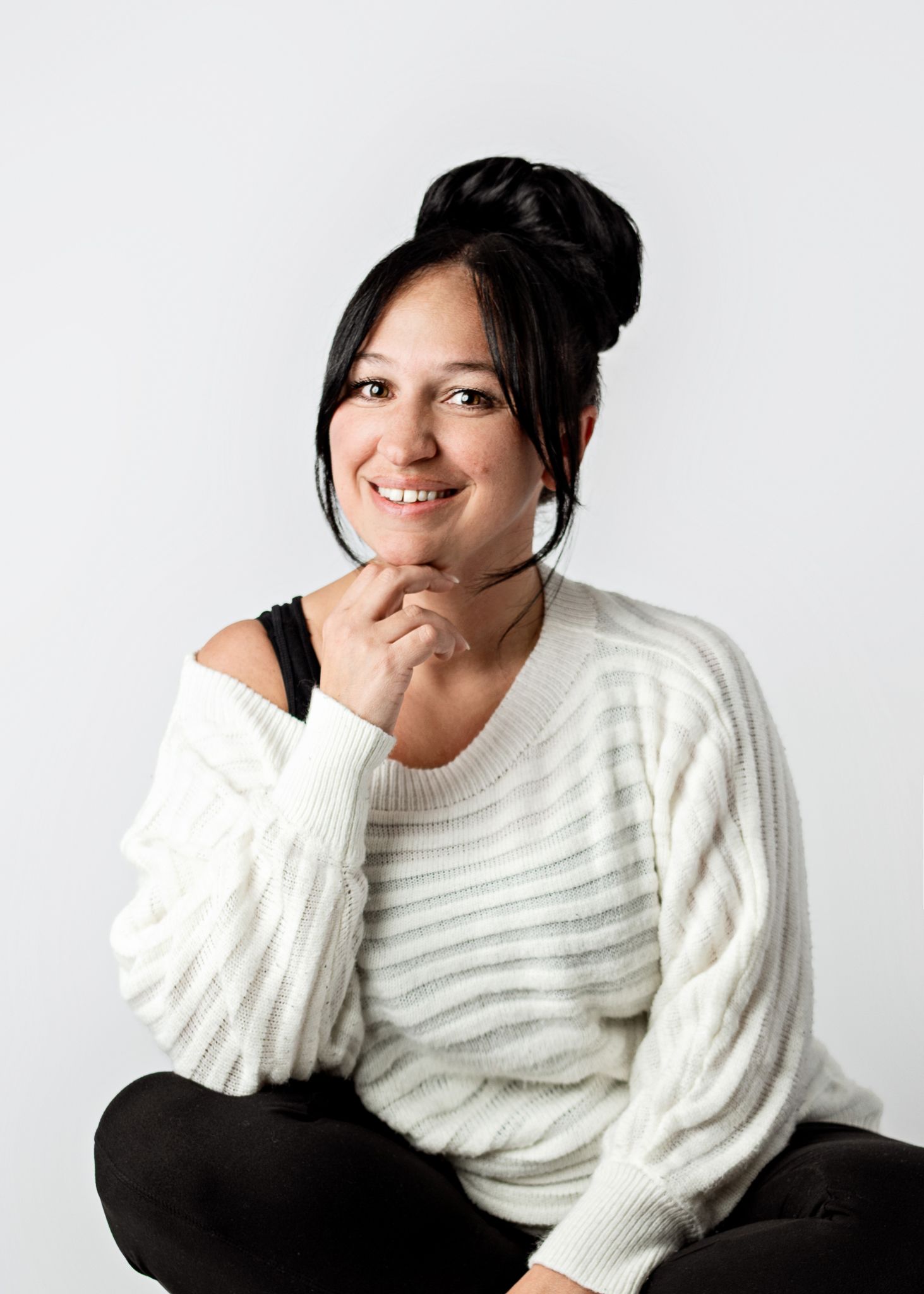 Person wearing a cozy white knit sweater sits relaxed with hand under chin against white background.