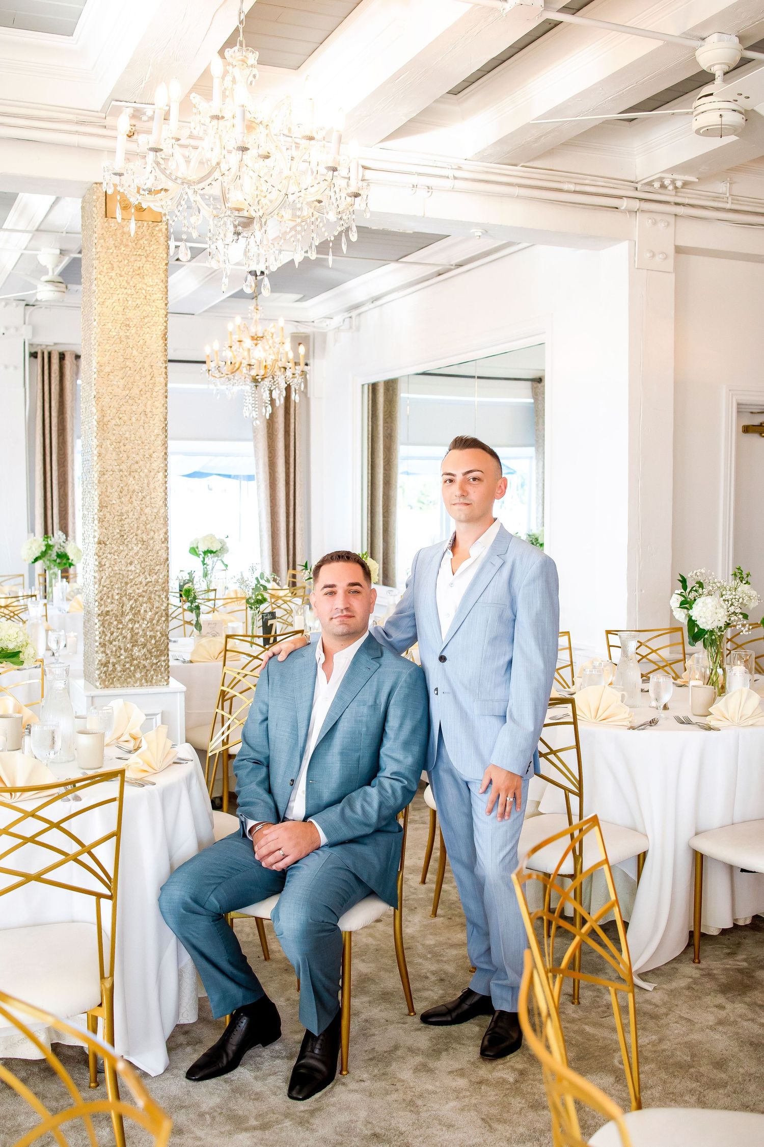 A softly lit elegant wedding venue with golden chairs, white linens, and chandeliers creating a luxurious atmosphere.