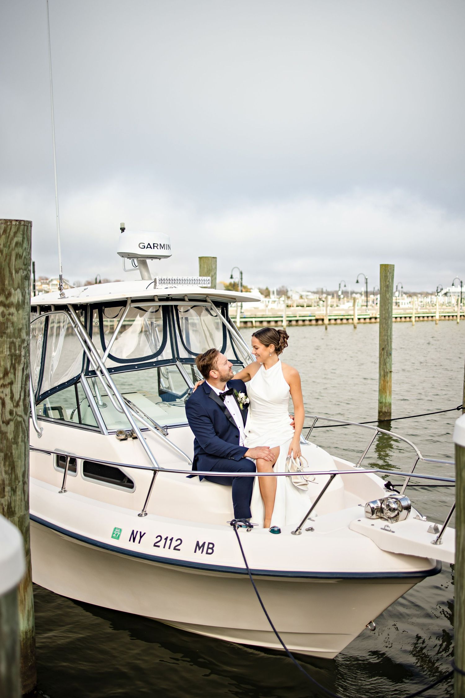 Bride and groom share a romantic moment on a white motorboat docked in a marina on their wedding day.