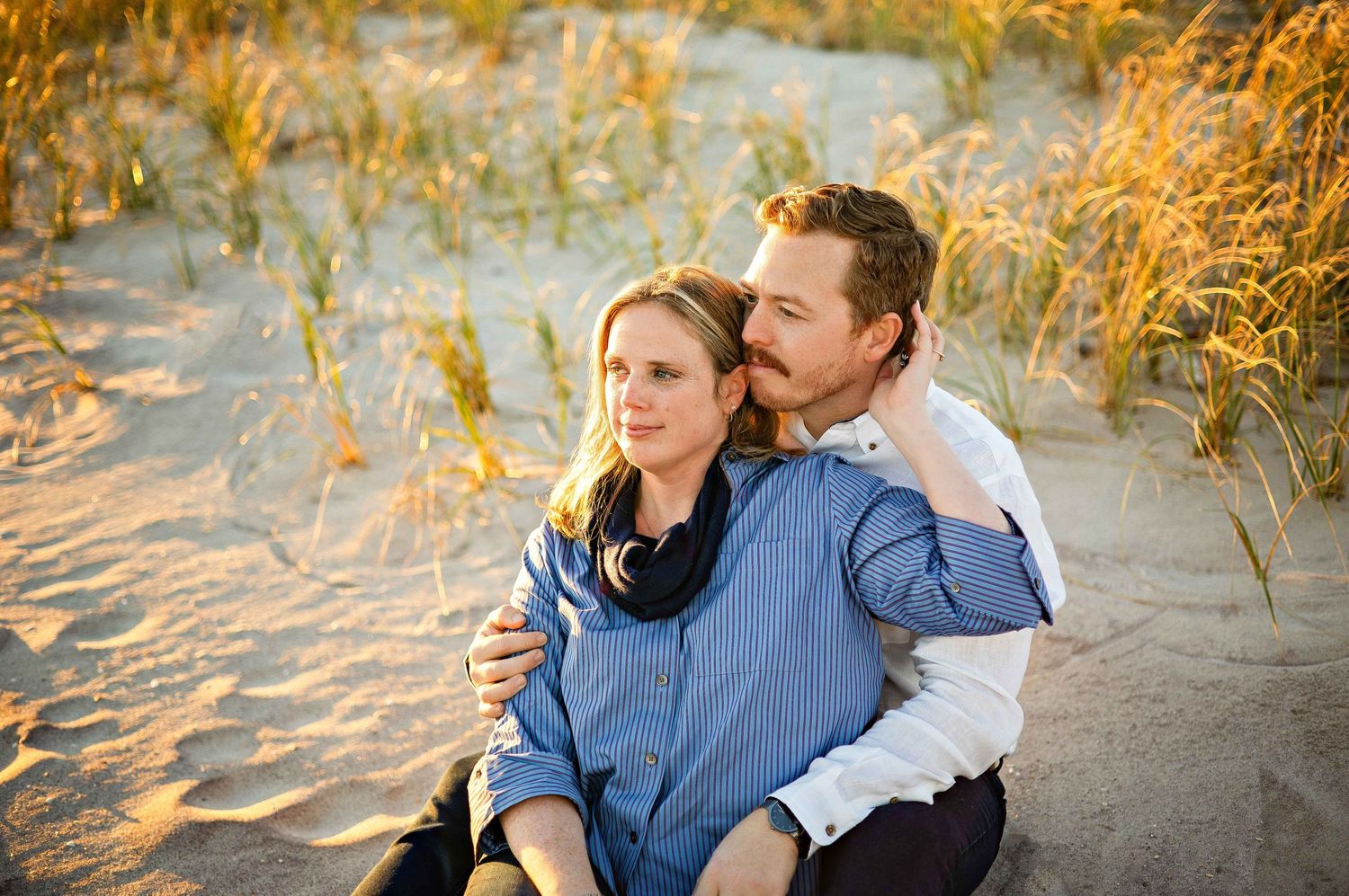 Couple sharing tender moments on a sandy beach during golden hour as sunlight creates warm, romantic atmosphere.