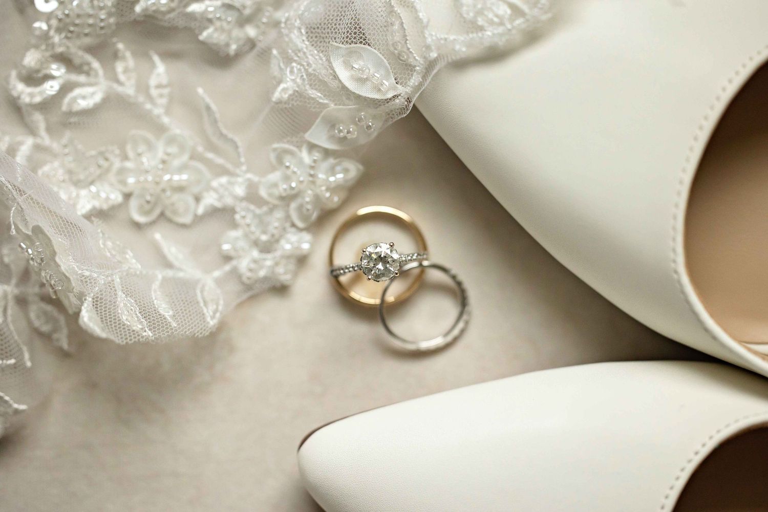 Wedding rings rest on delicate white lace next to elegant ivory accessories in a romantic bridal setting.