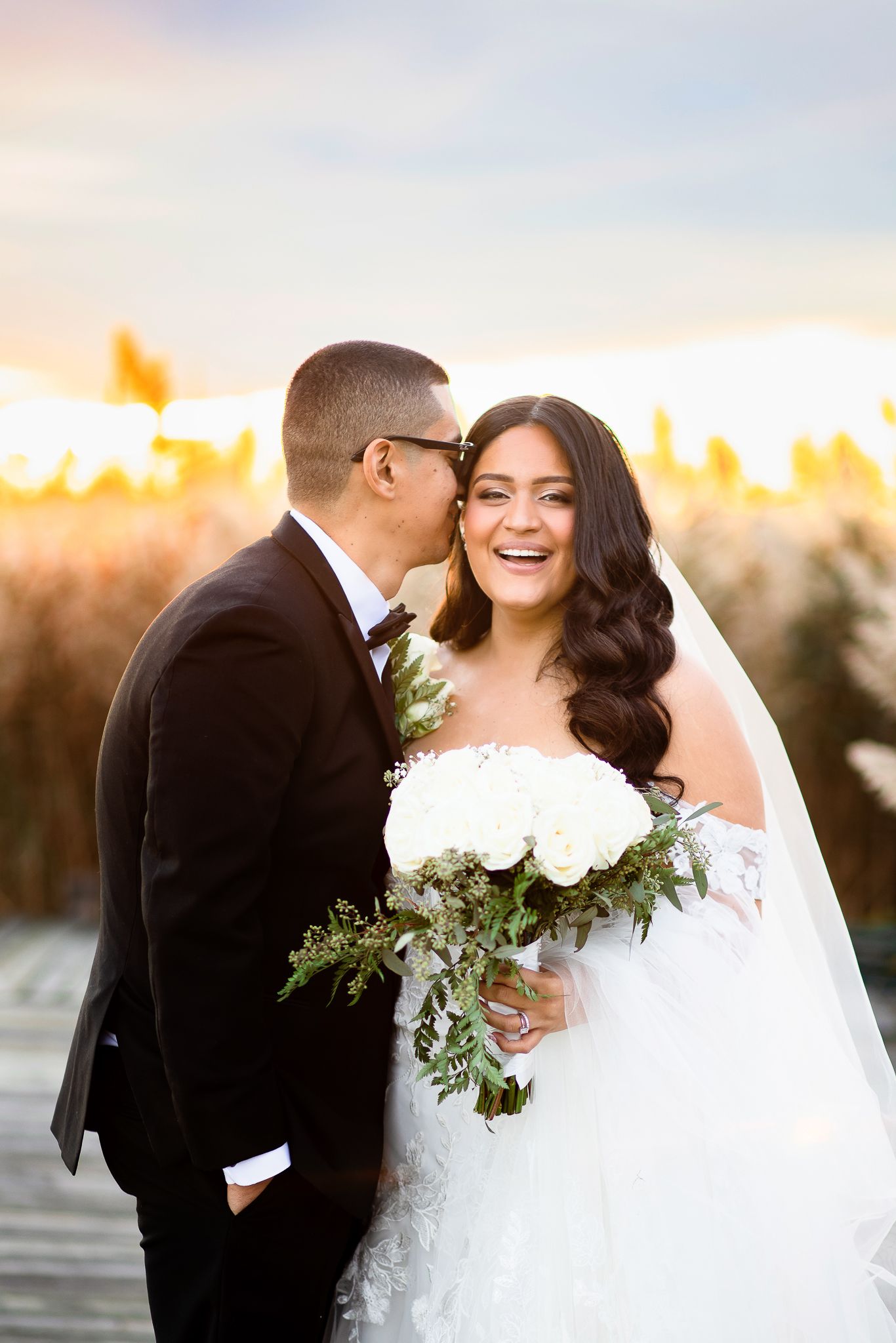 A joyful wedding moment captured at sunset with a stunning white bouquet and elegant dress.