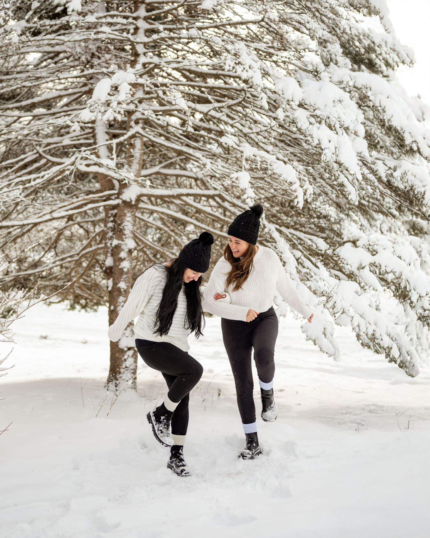 Two people playing and throwing snow at each other in a snowy winter forest setting.