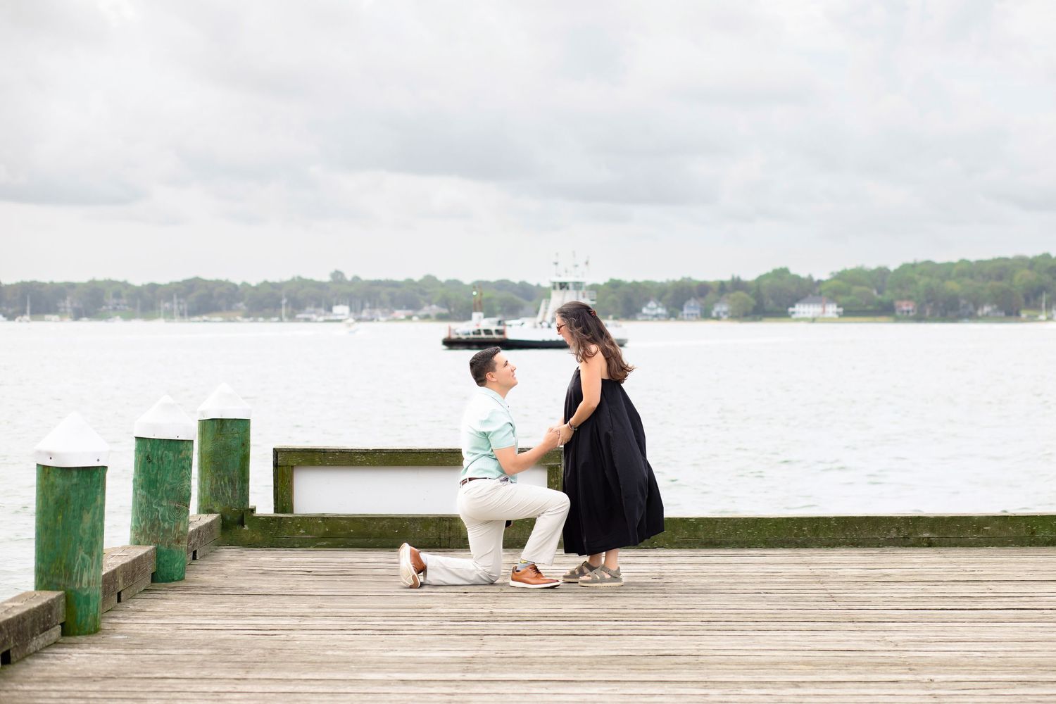 A couple sits together on a wooden dock overlooking a serene lake on a cloudy day.