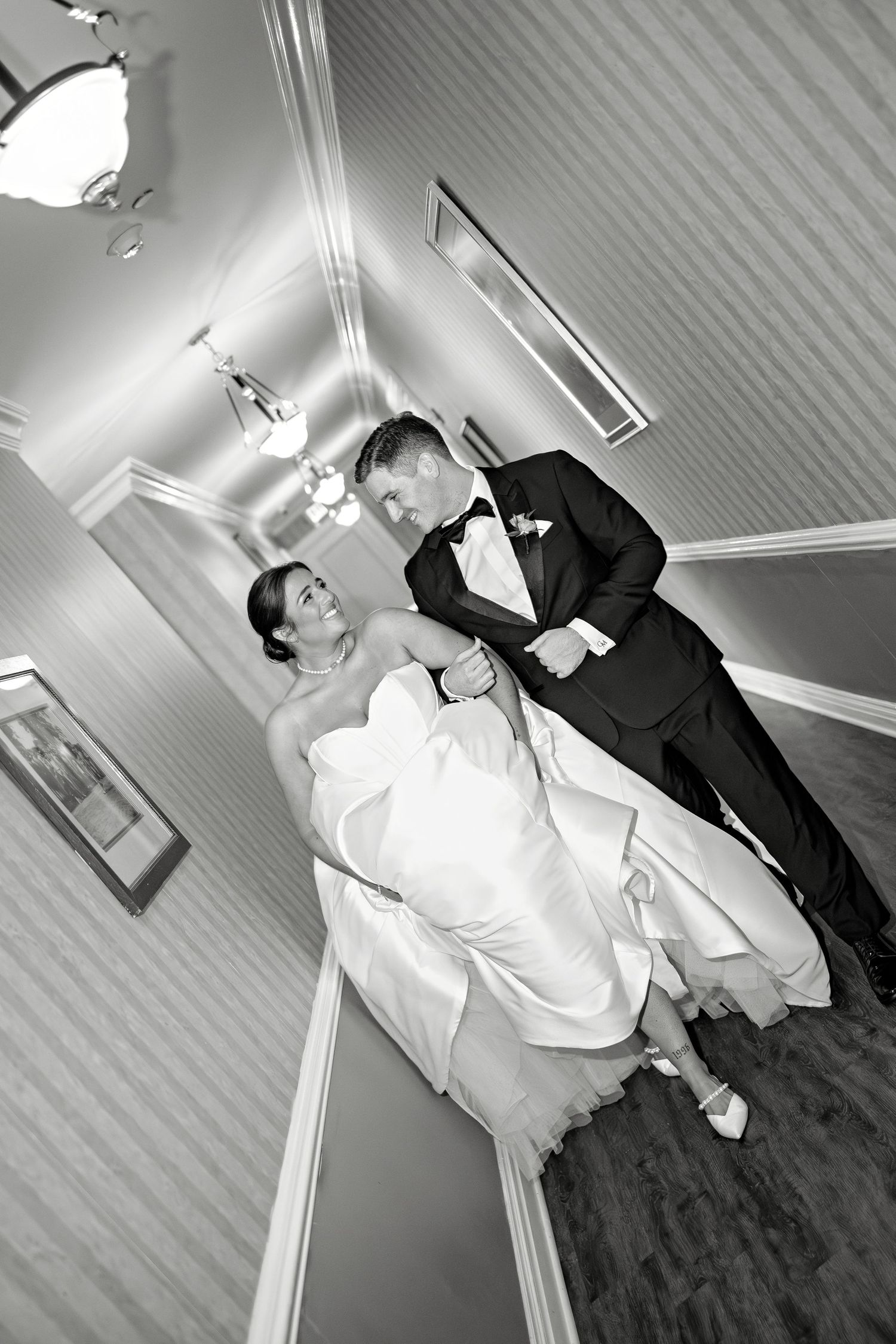 Black and white photo of a bride and groom holding hands in an elegant hallway on their wedding day.