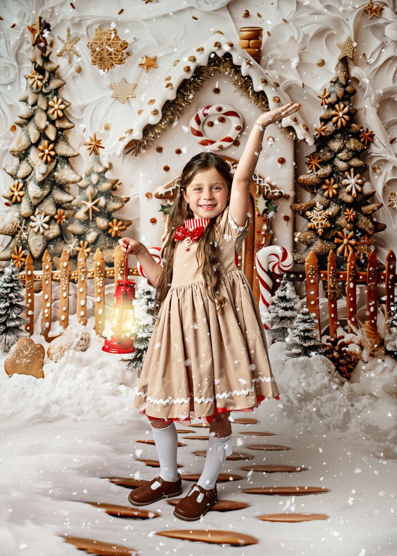Smiling girl in holiday dress holds glowing lantern with arm raised in magical gingerbread Christmas scene.