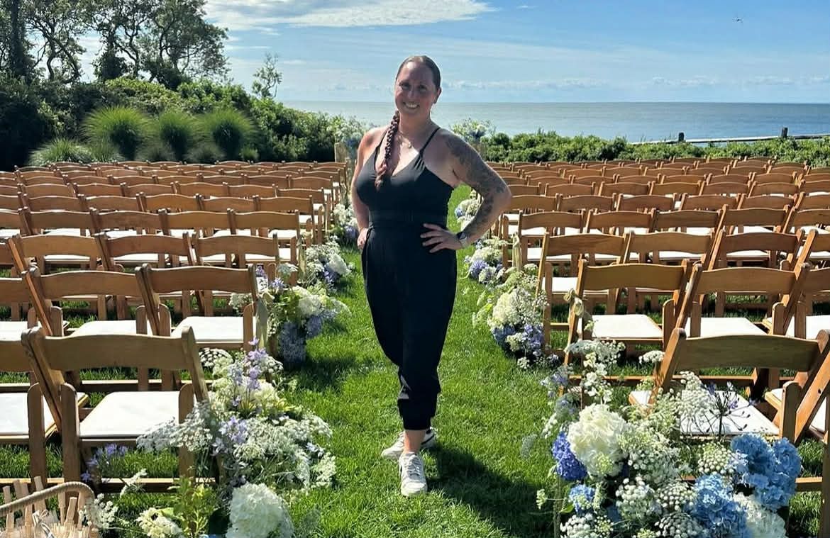 Rustic wooden chairs arranged outdoors for a wedding ceremony with ocean views and white floral decorations.