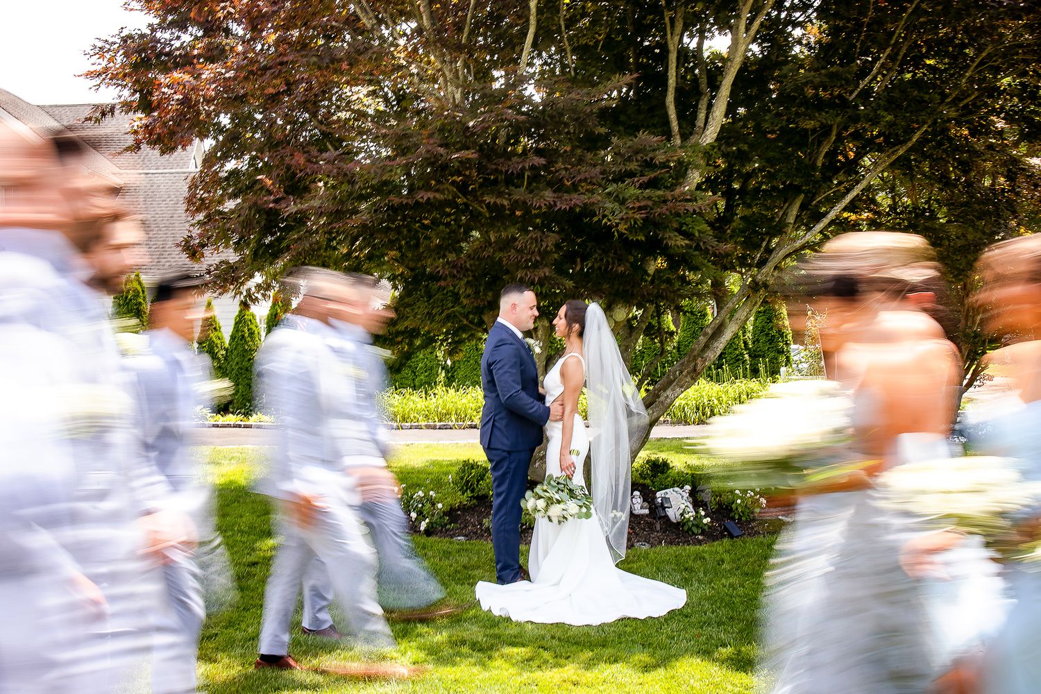 Creative wedding photo with motion blur of guests walking while couple stands still in garden ceremony setting.