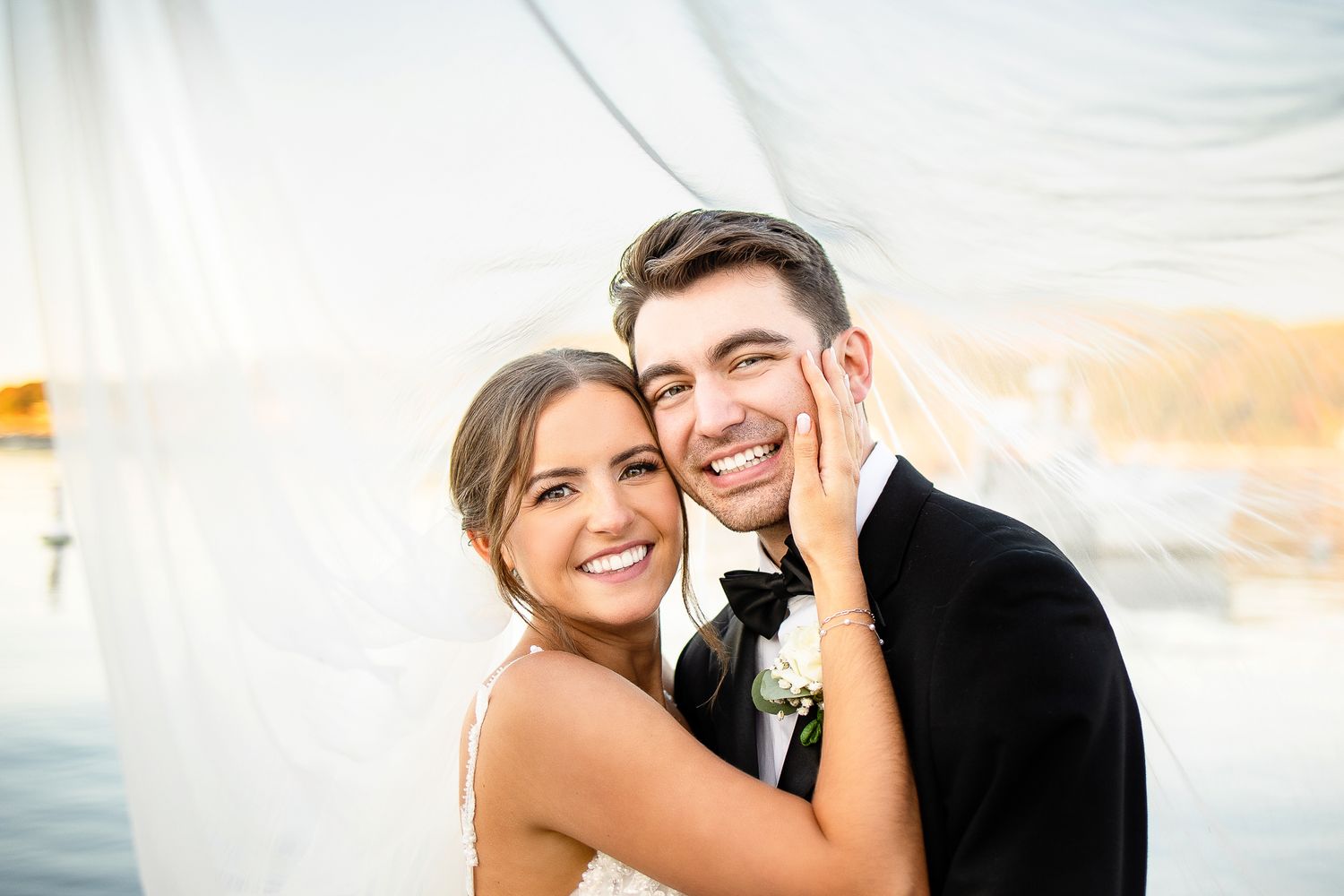 Happy wedding couple embraces on a boat during golden hour sunset with water and sky in background.