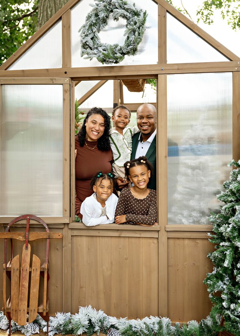 Happy family of five peeks through the open door of a festively decorated Christmas greenhouse.