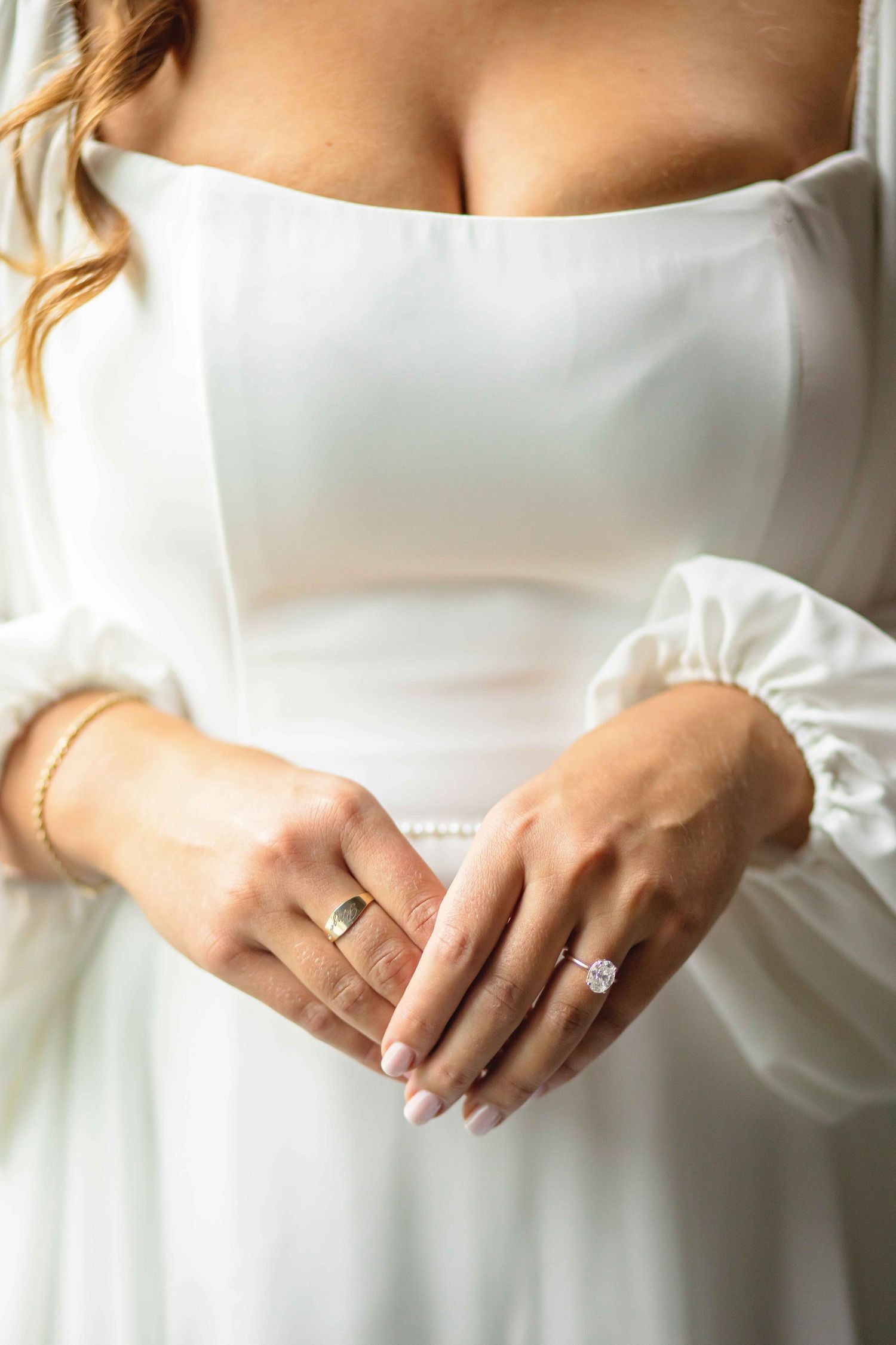 Close-up view of hands wearing elegant wedding rings against a white dress background.