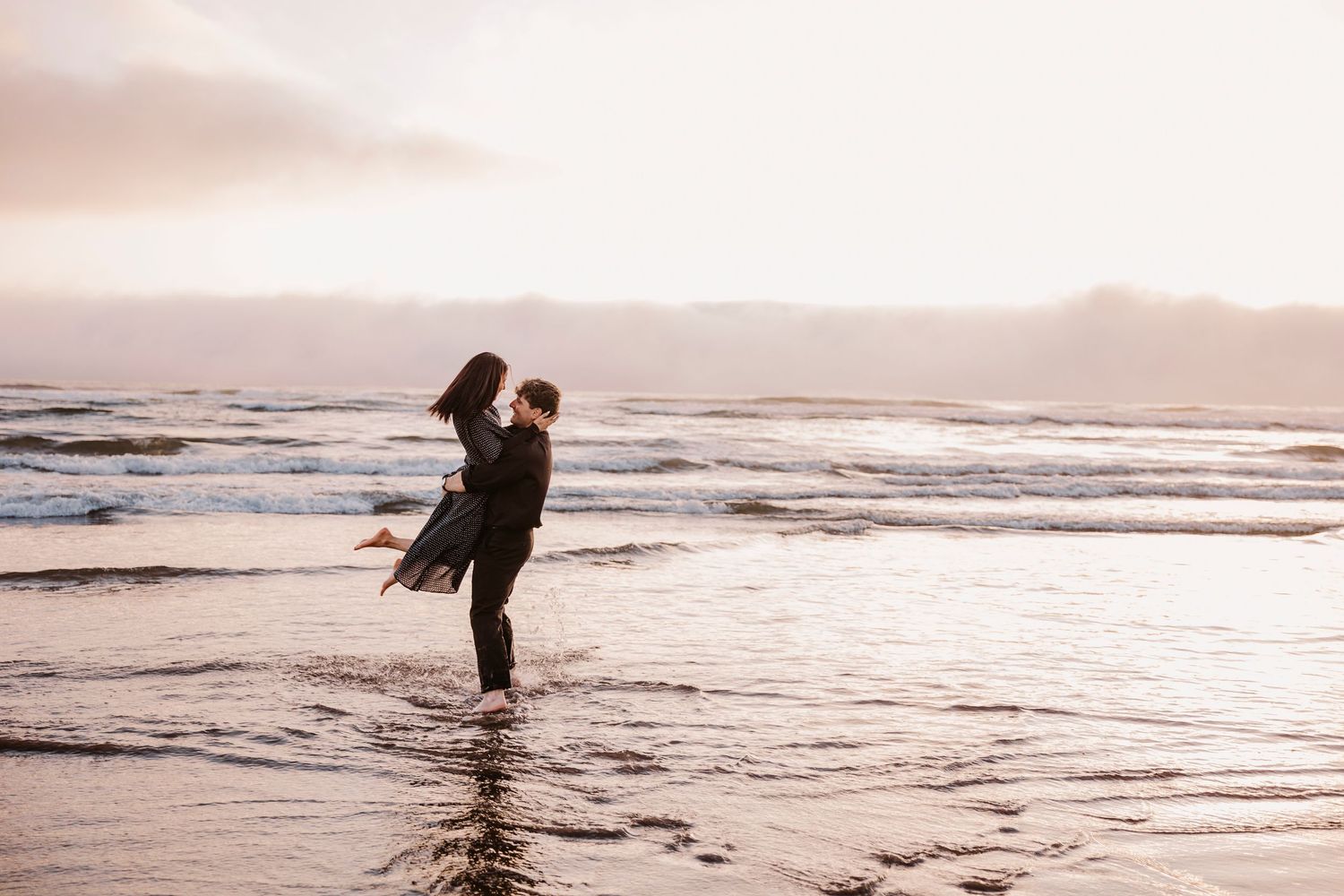 A silhouetted couple embraces in shallow ocean water during sunset.