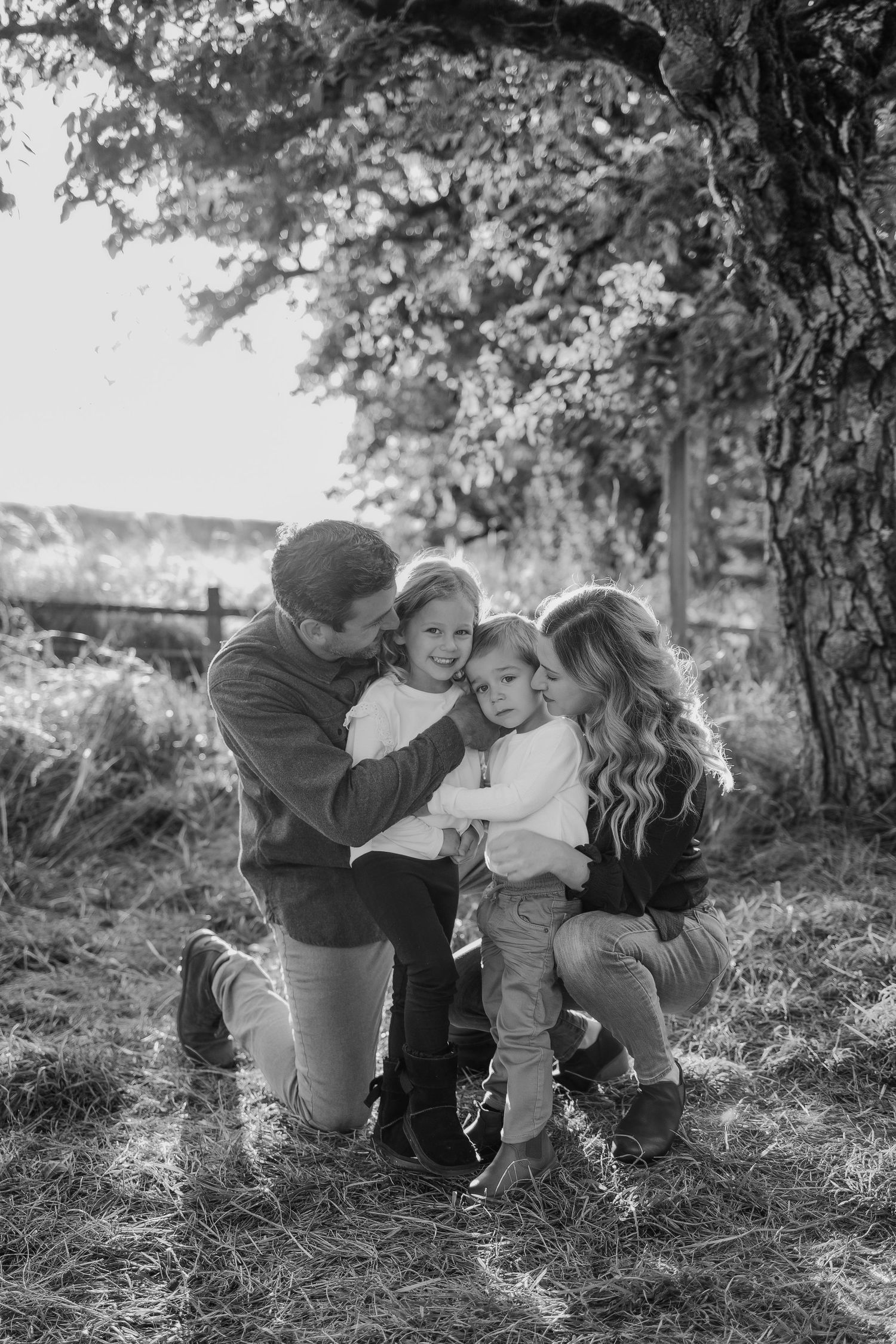 A family shares tender moments together in a sunlit forest setting.