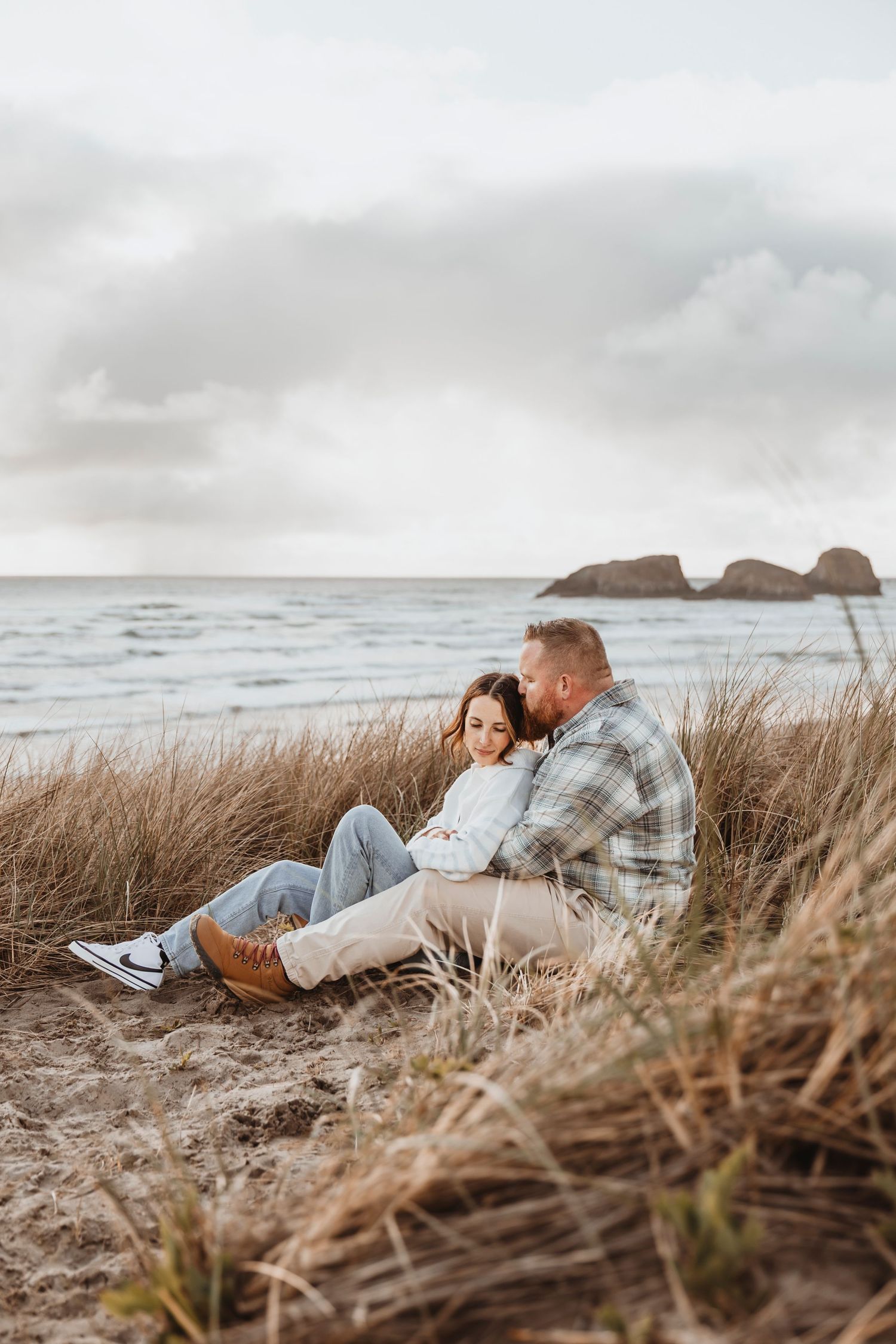 Couple lying in beach grass during golden hour coastal photoshoot.