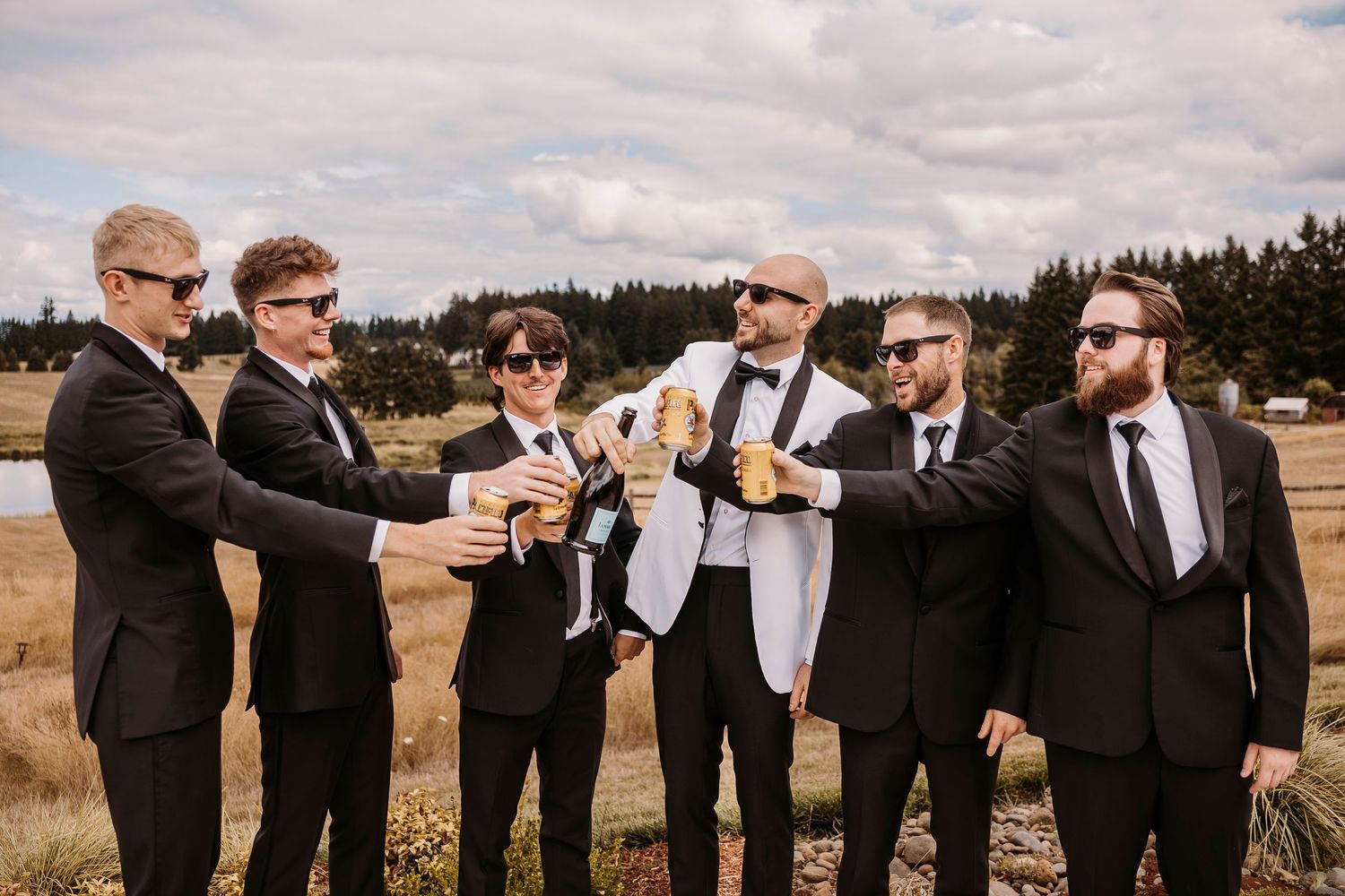 Wedding party in black suits posing in a line outdoors for group photos.