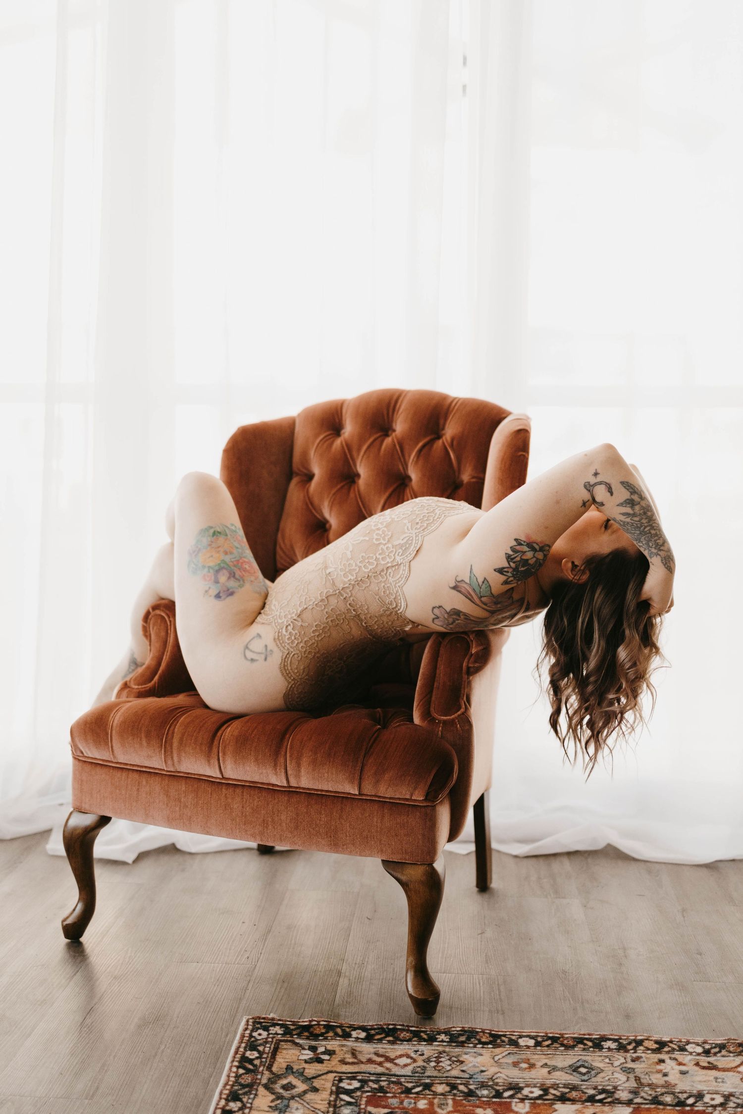 Artistic pose on vintage brown tufted settee with sheer curtain backdrop.