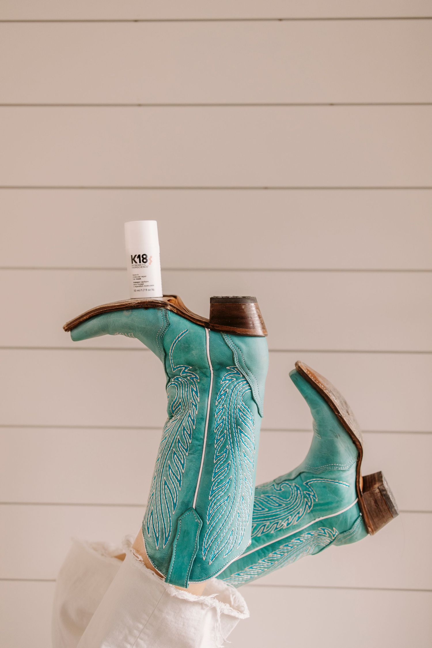 Turquoise hair styling cape with intricate pattern detail displayed against white paneled wall.