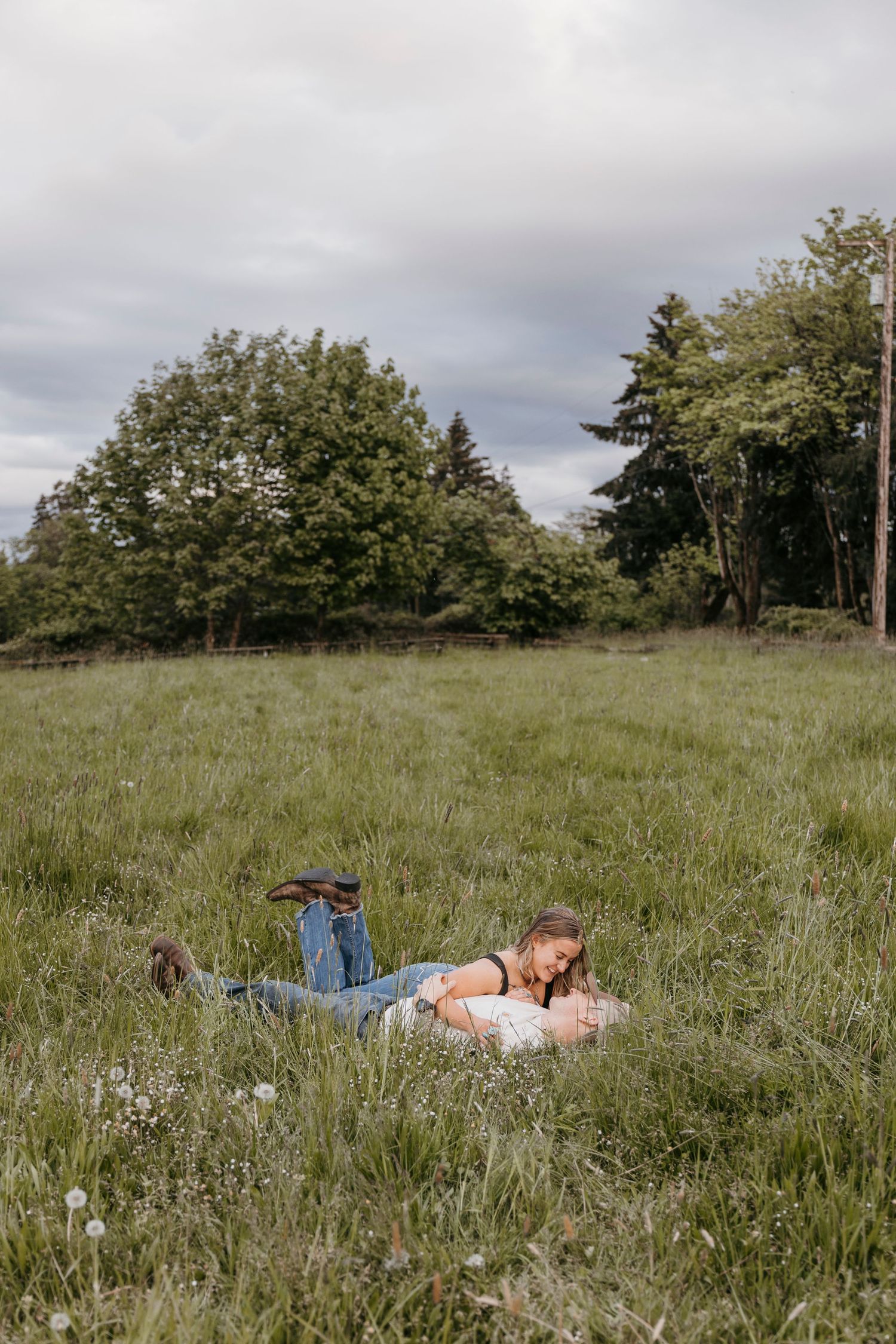 Couple lying together in tall grass meadow on cloudy summer day.