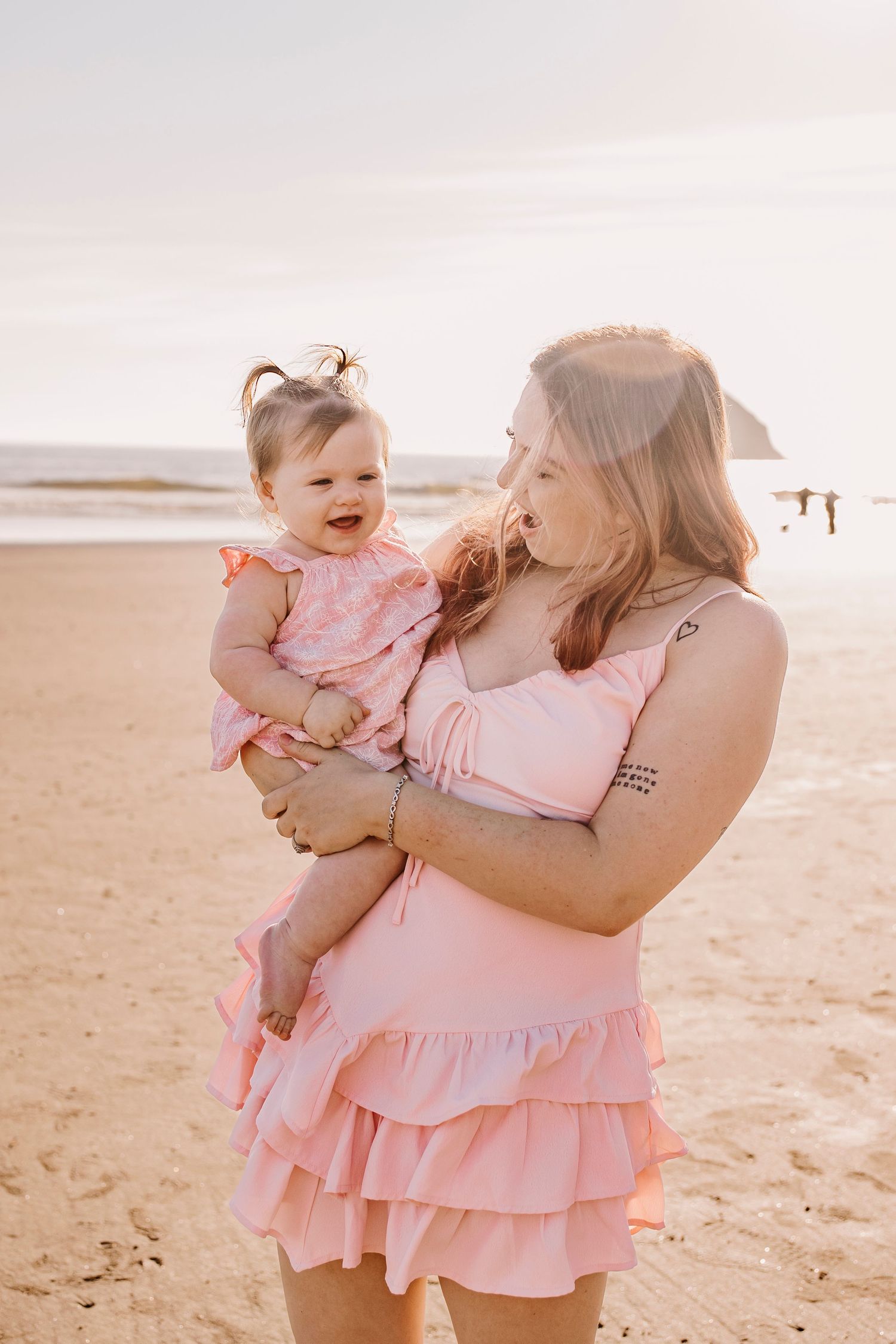 A joyful moment between parent and baby in matching pink outfits on a sunny beach.