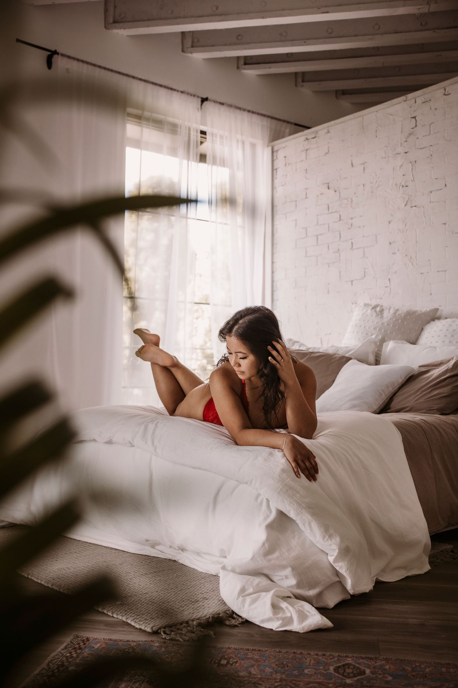 Person lying on white bedding in sunlit room with brick walls.