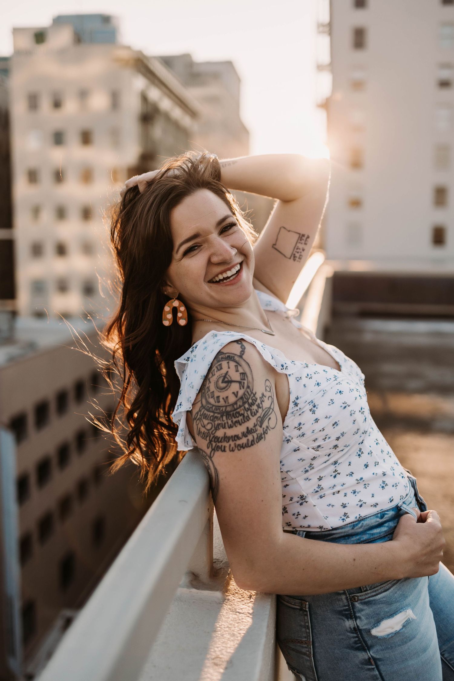 Rooftop portrait at sunset showing joyful expression and visible tattoo art.