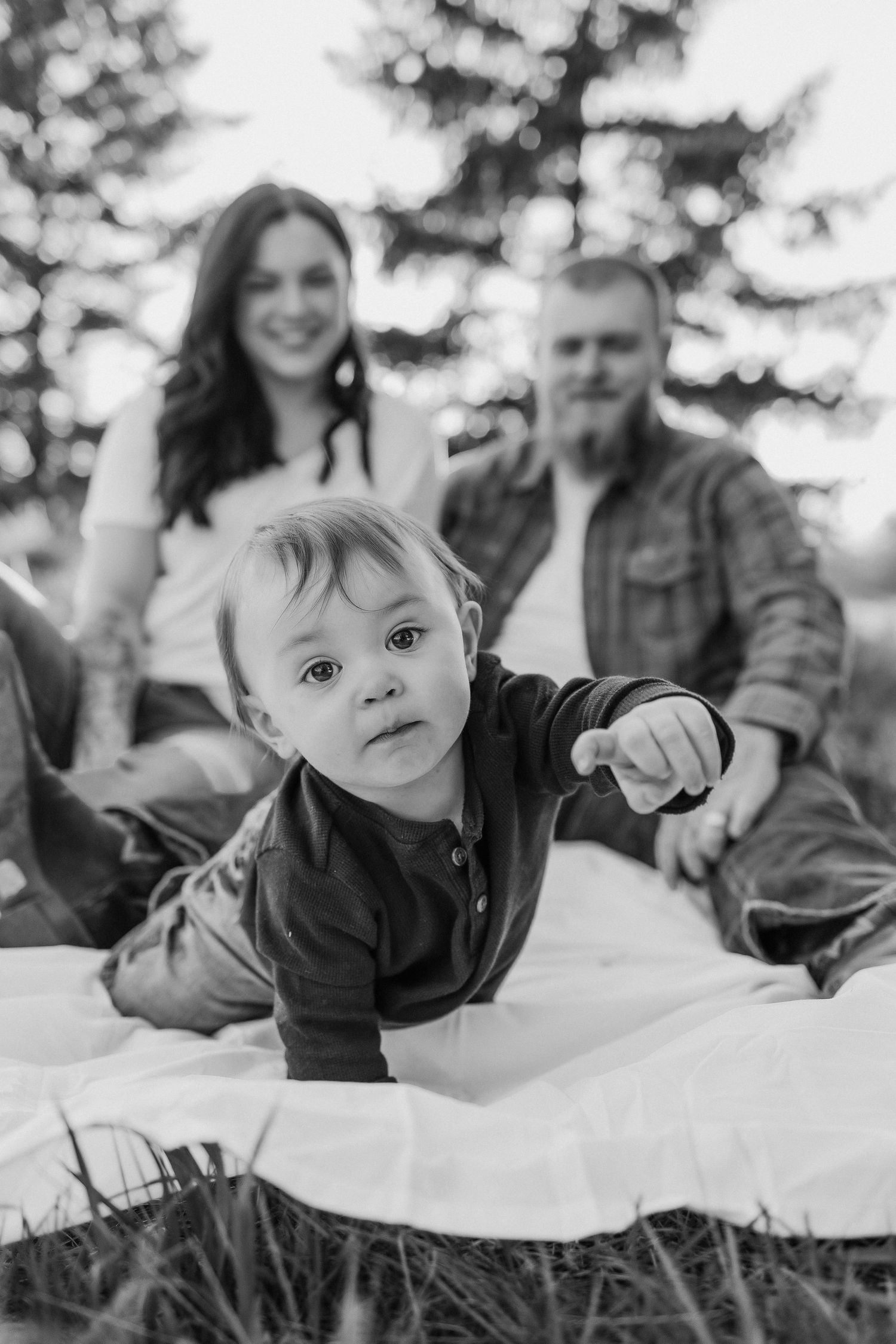 Black and white family portrait with evergreen trees in background.