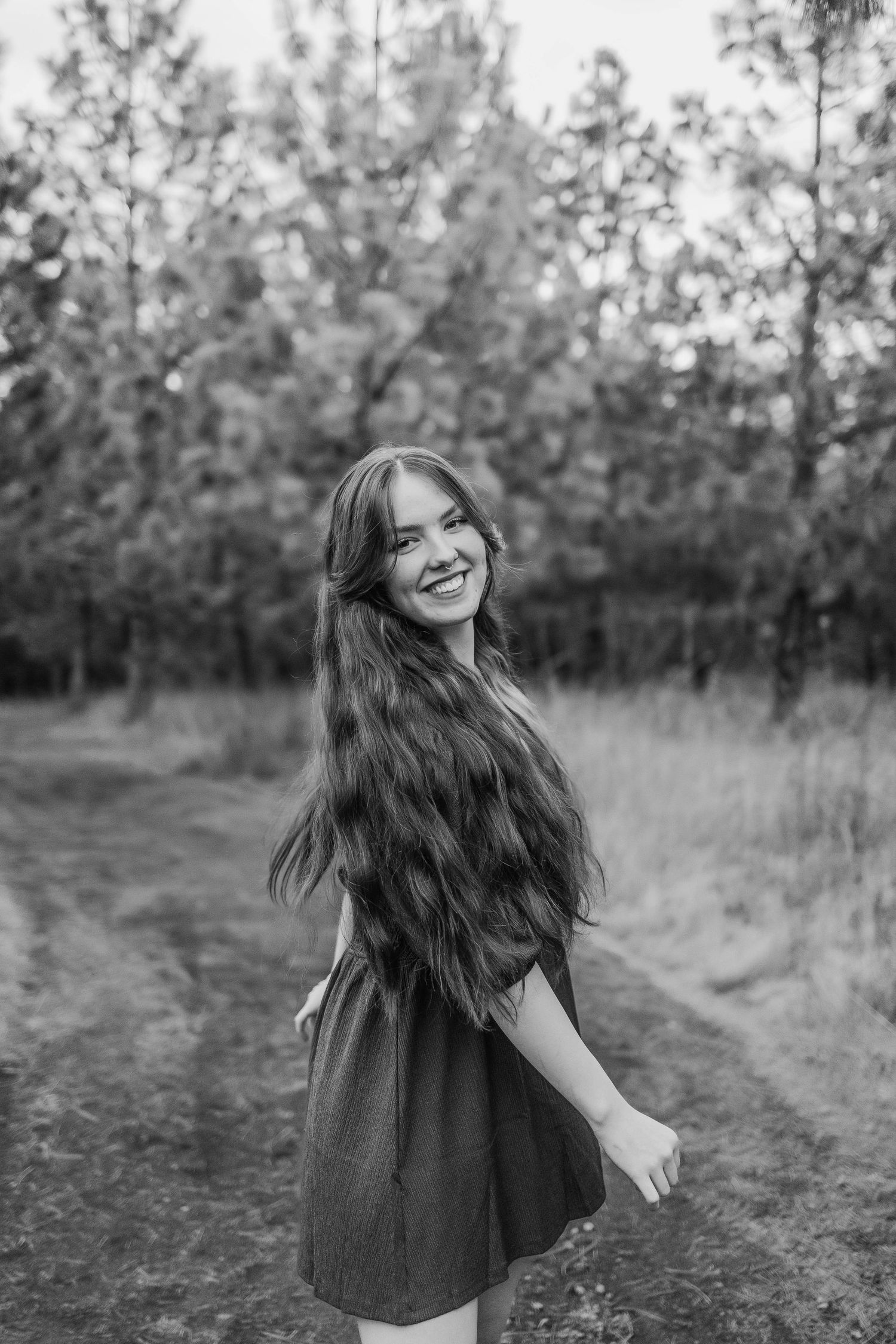 Black and white portrait of someone with flowing long hair twirling on a forest path.