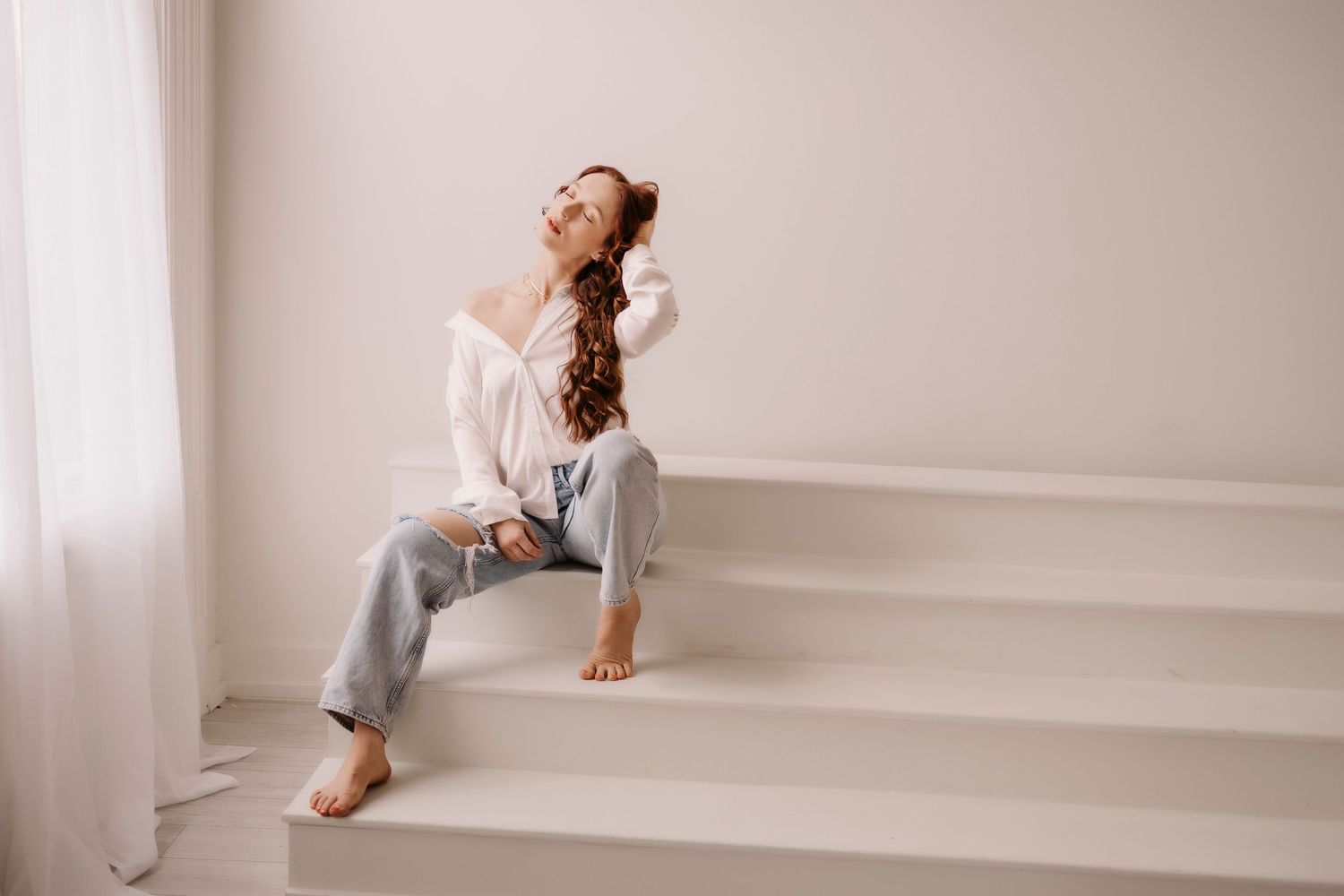 Casual indoor portrait on white stairs showing relaxed lounging pose in comfortable attire.